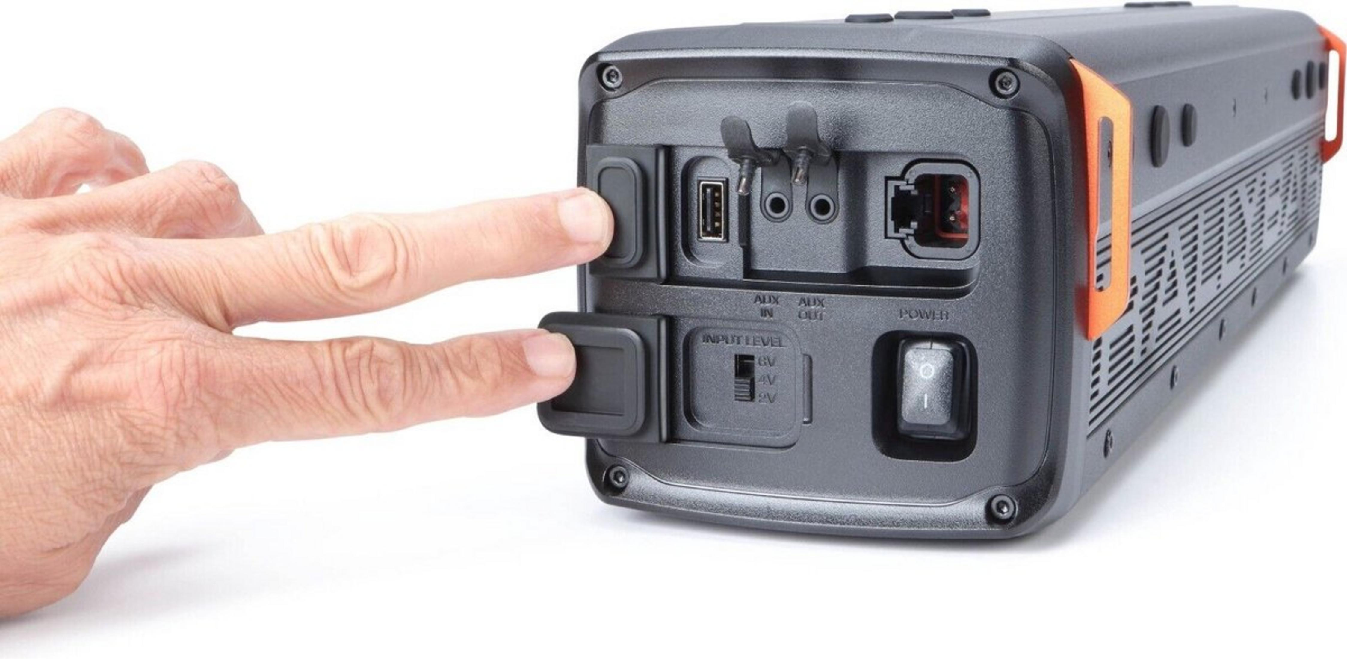 A hand presses a button on a black and orange device with ports.