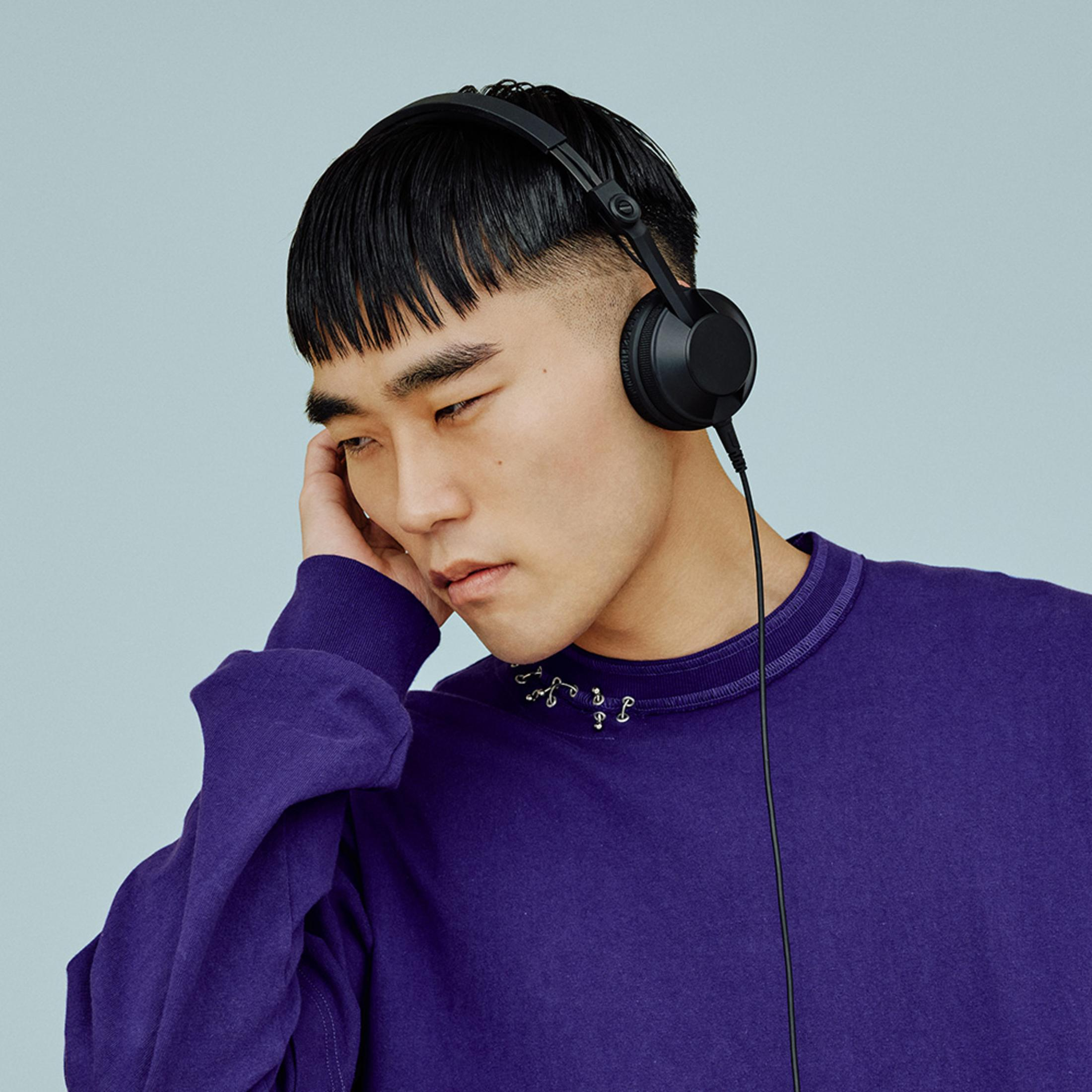 Młody mężczyzna w słuchawkach, dotykający ucha dłonią.