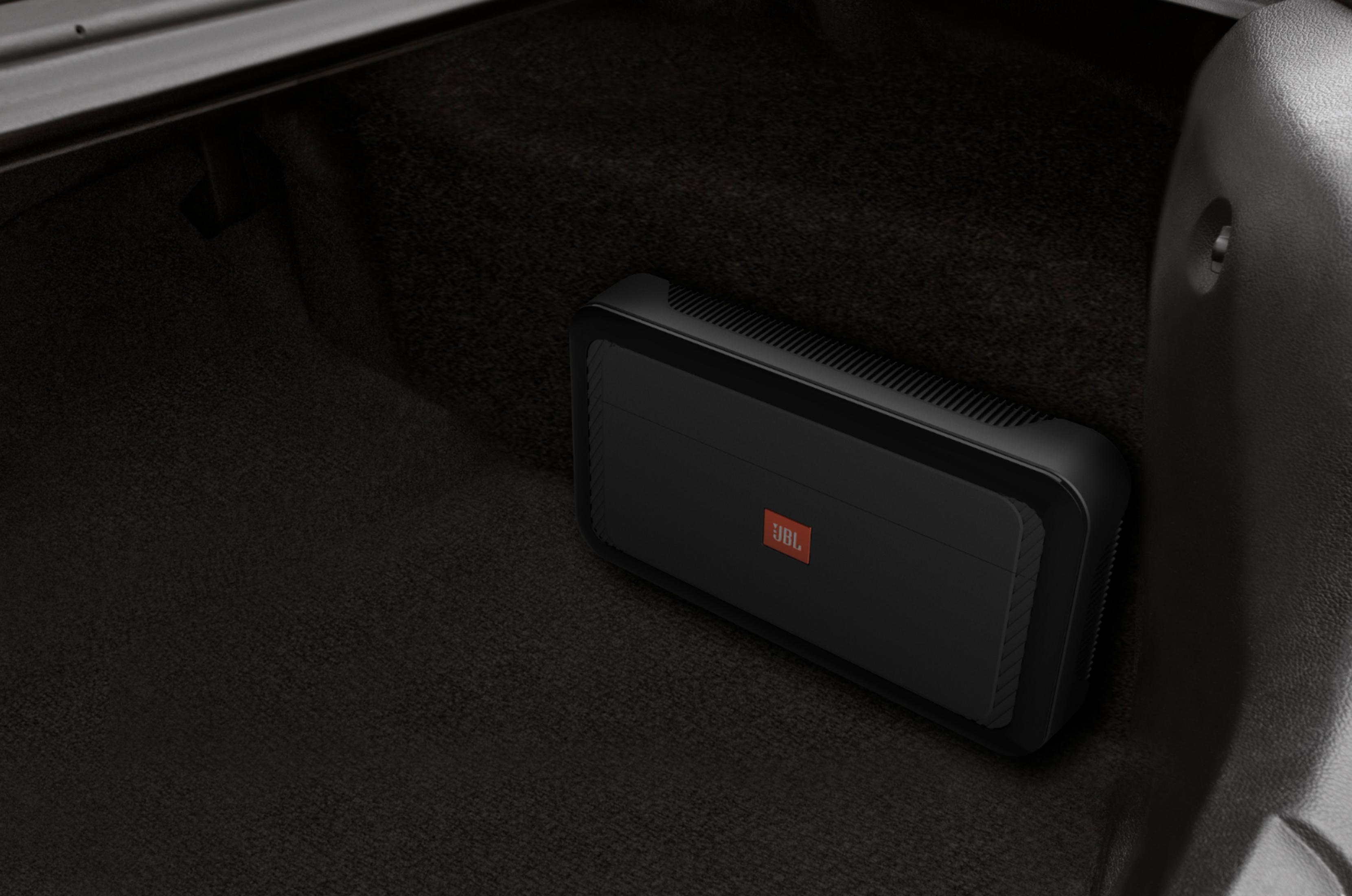 Ein schwarzer JBL-Verstärker liegt auf dem Teppich im Kofferraum eines Autos.