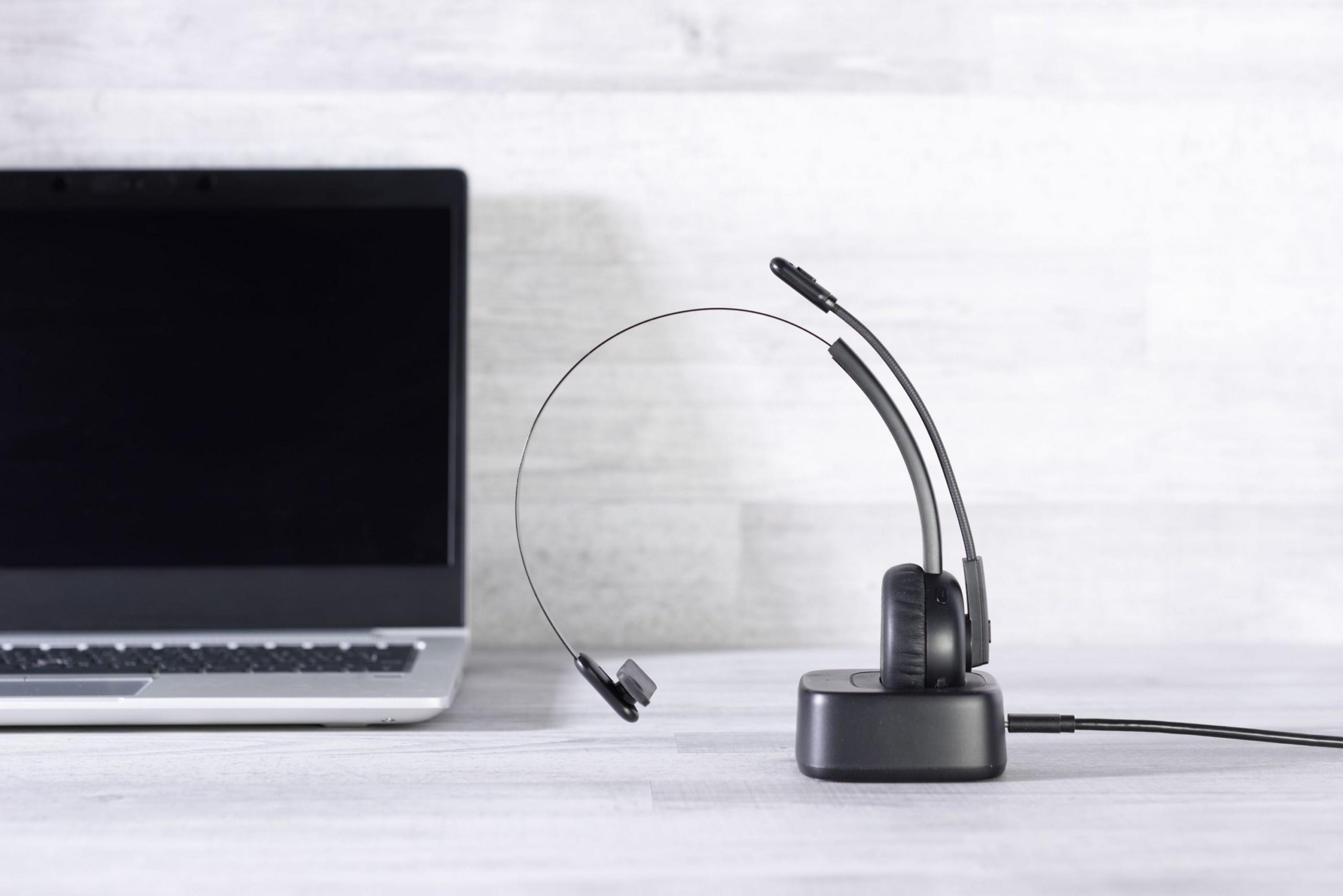 Ein Headset mit Mikrofon ruht auf einer Ladestation neben einem Laptop.