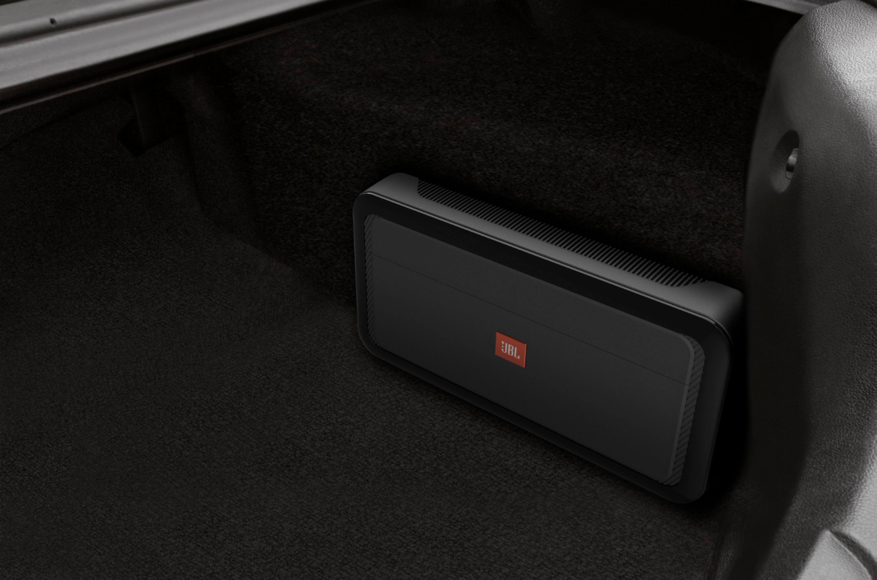 Schwarzer JBL-Verstärker im Kofferraum auf dunklem Teppich.