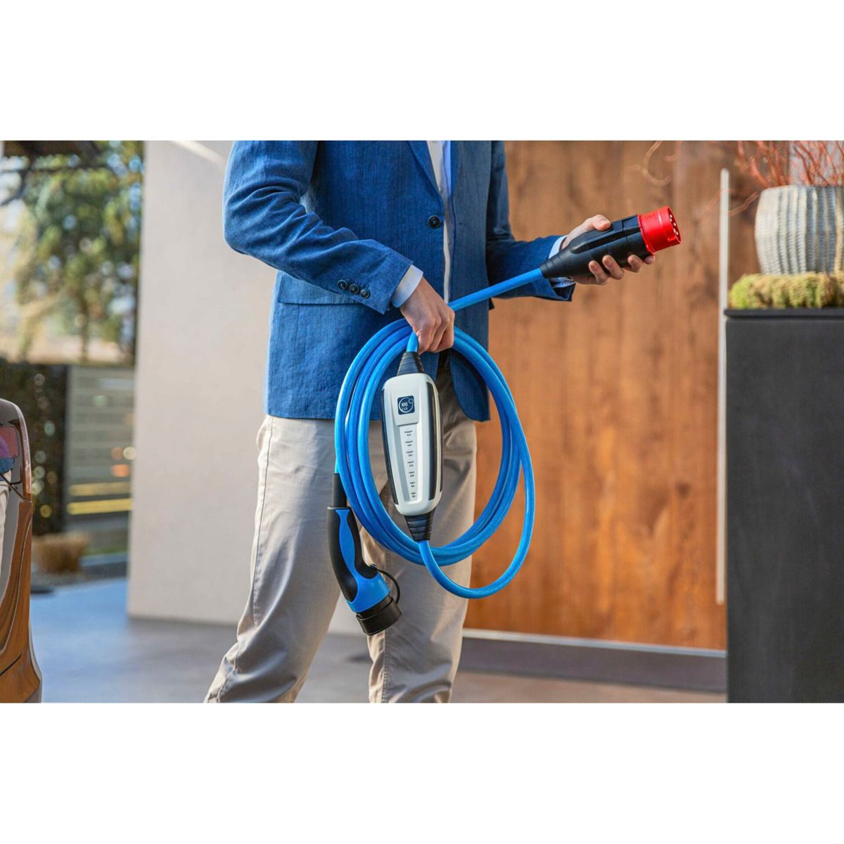 Mann in blauem Sakko hält ein blaues Ladekabel mit weißem Kasten und rotem Stecker.