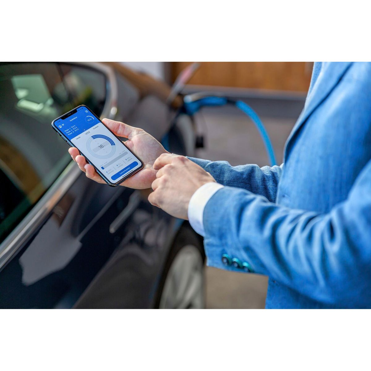 Mann in blauem Anzug hält Smartphone mit Lade-App neben Elektroauto.