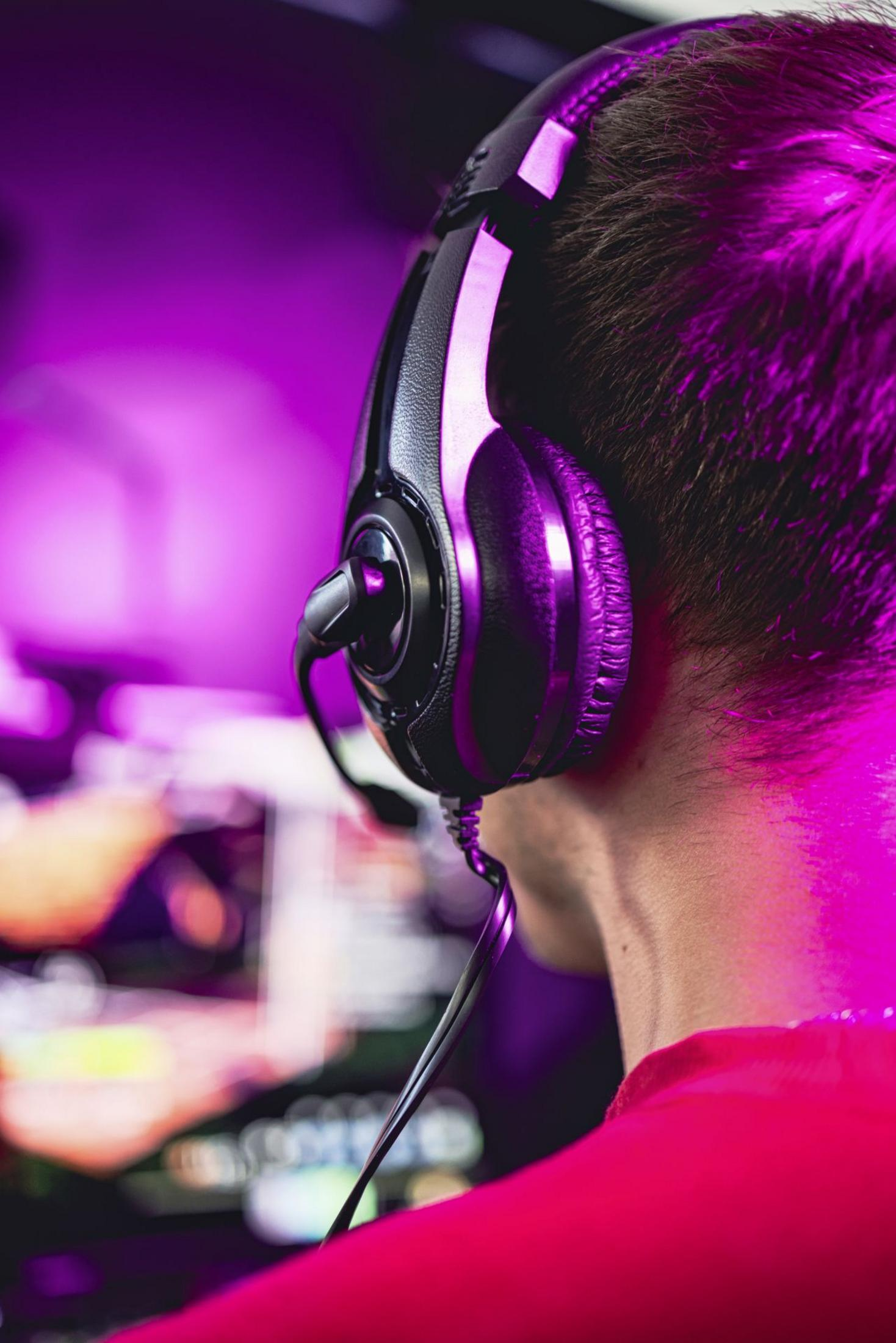 A person wearing headphones and a red shirt, illuminated by purple light.