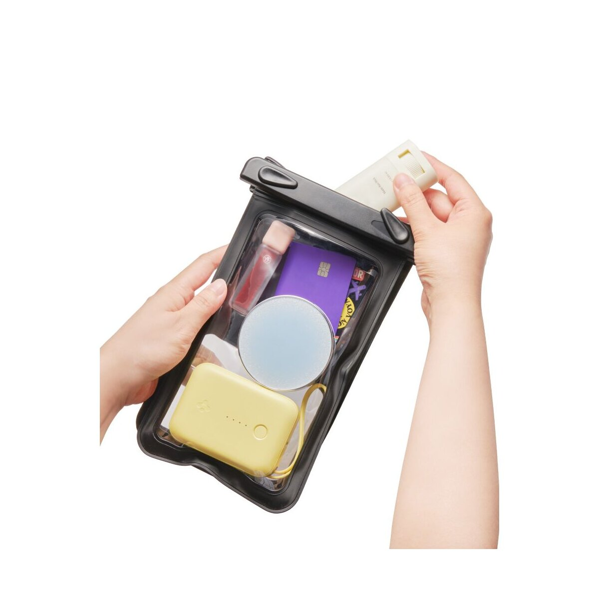 Mani riempiono una pochette trasparente con rossetto, carta, specchio e power bank.