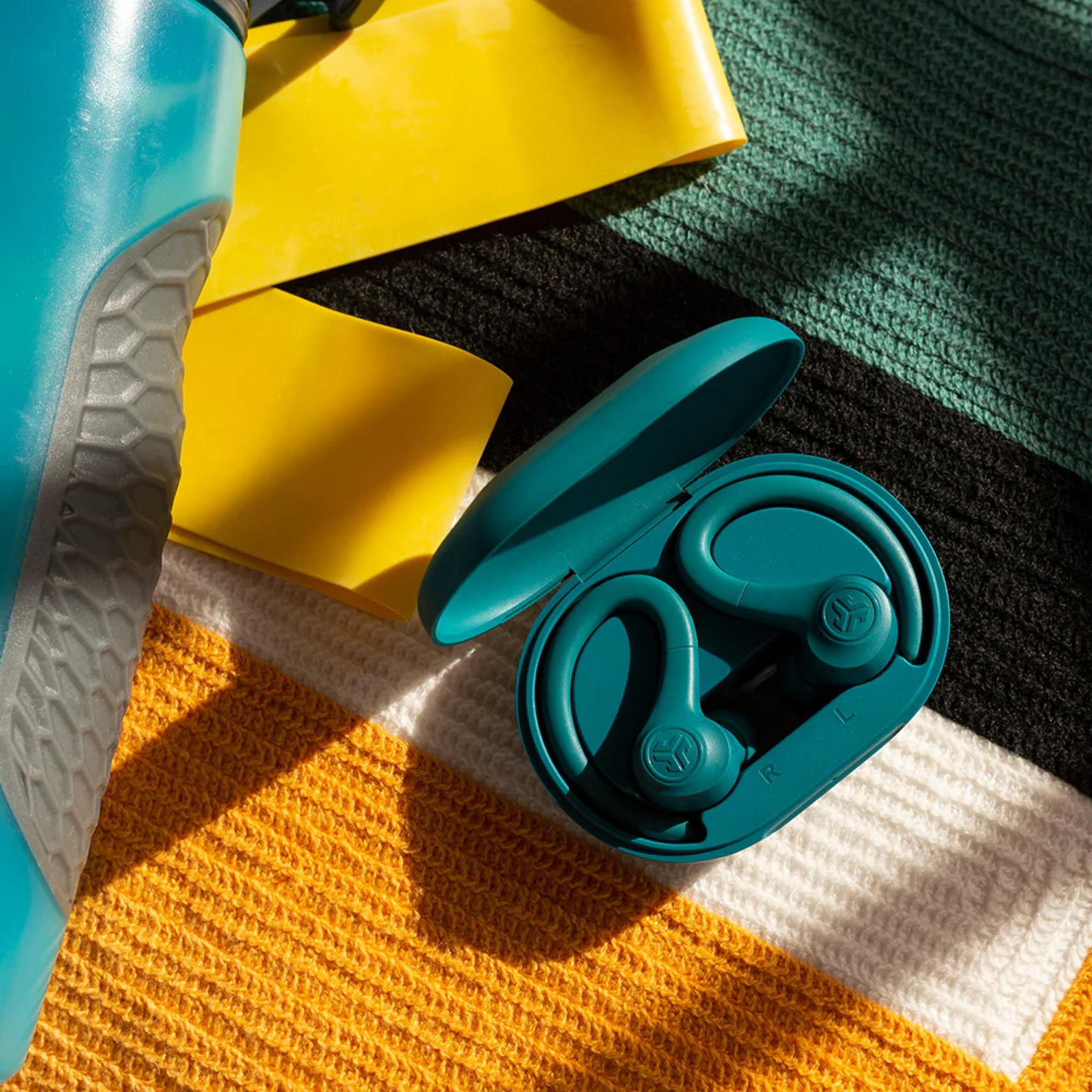 Turkusowe słuchawki w etui leżą na pasiastym kocu z żółtymi taśmami.