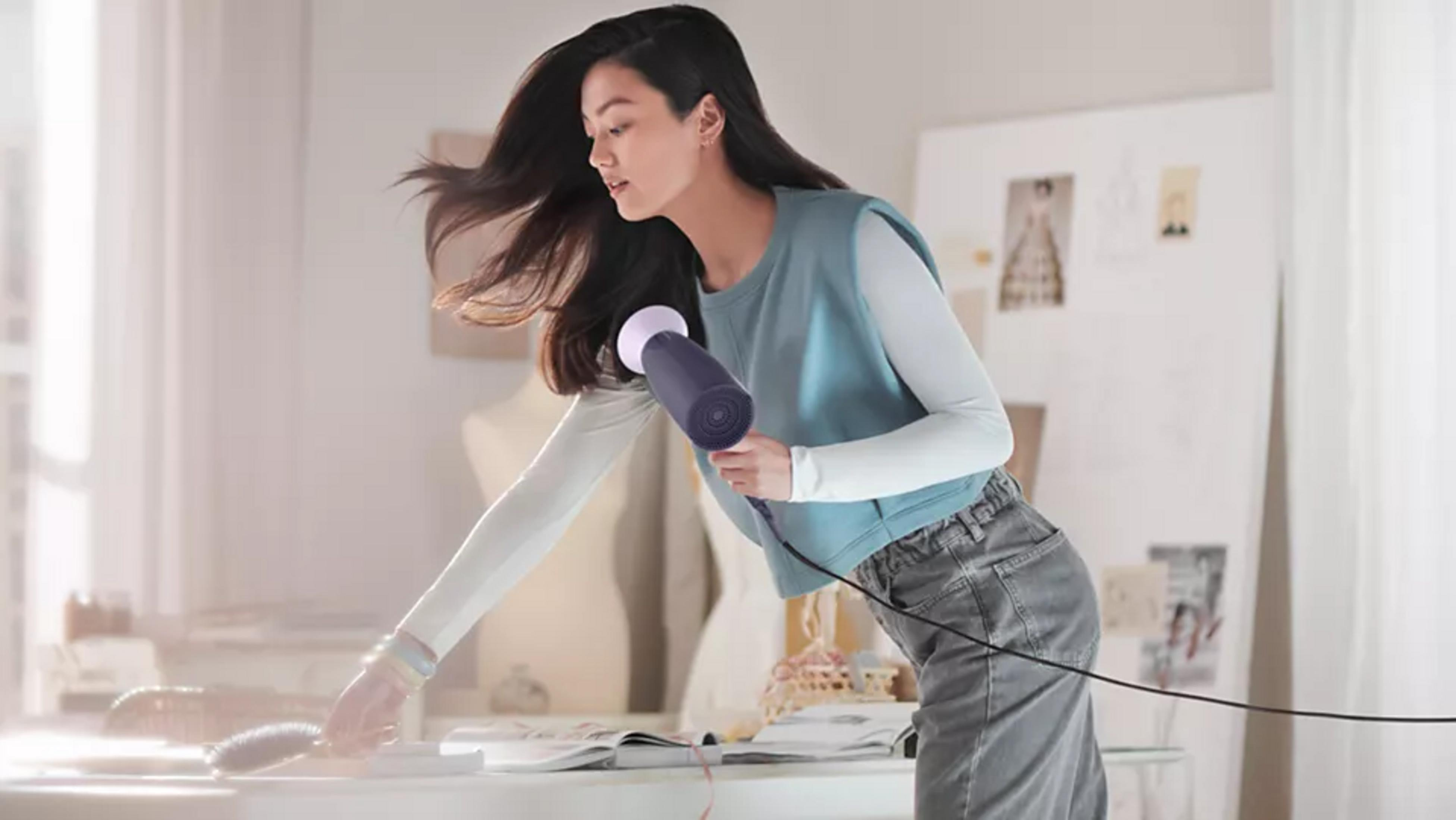 Kobieta suszy długie, ciemne włosy fioletową suszarką.