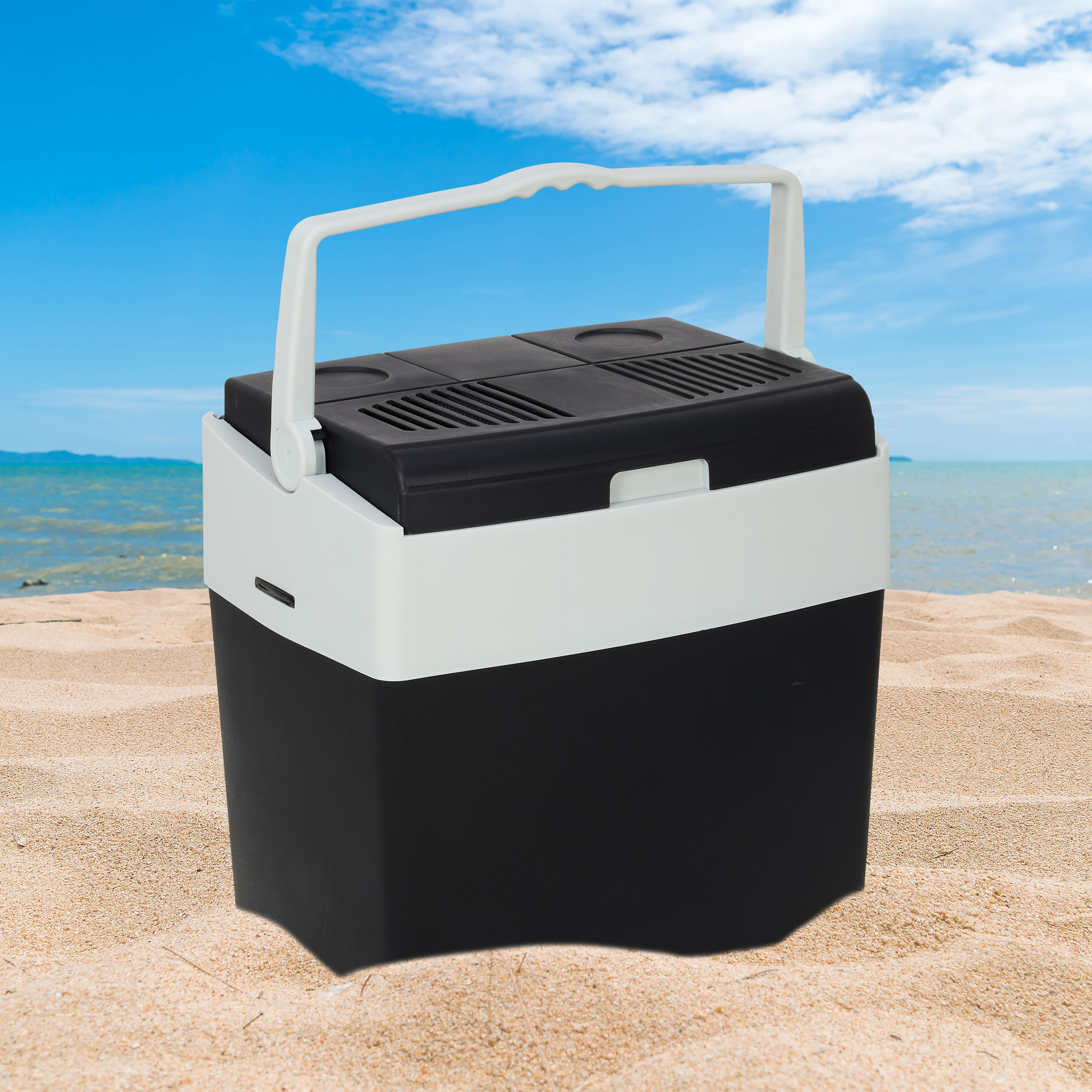 A black and white cooler sits on a sandy beach with the ocean and blue sky.