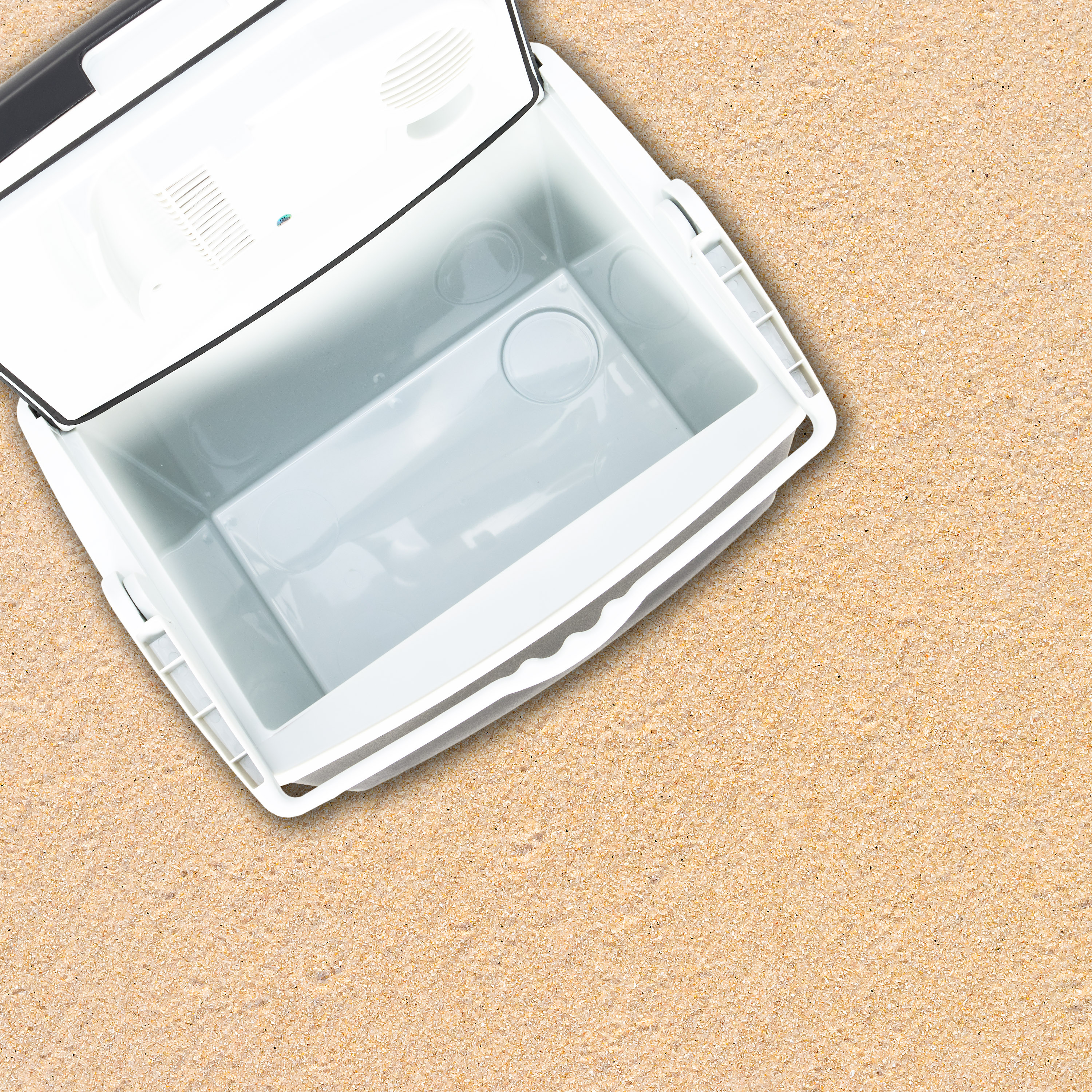 An open white cooler box on sand.