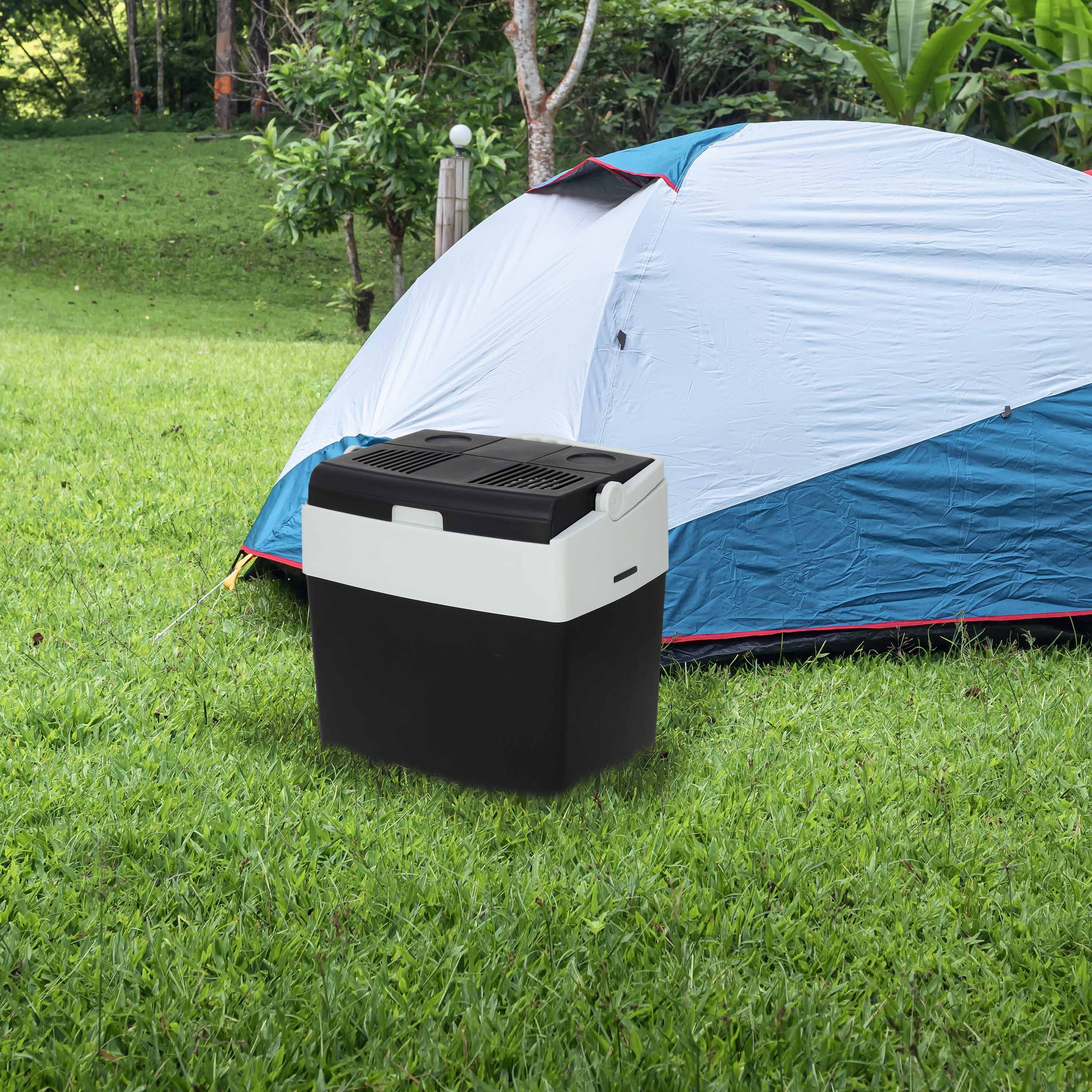 A black and white cooler sits in front of a blue and white tent on a grassy lawn.