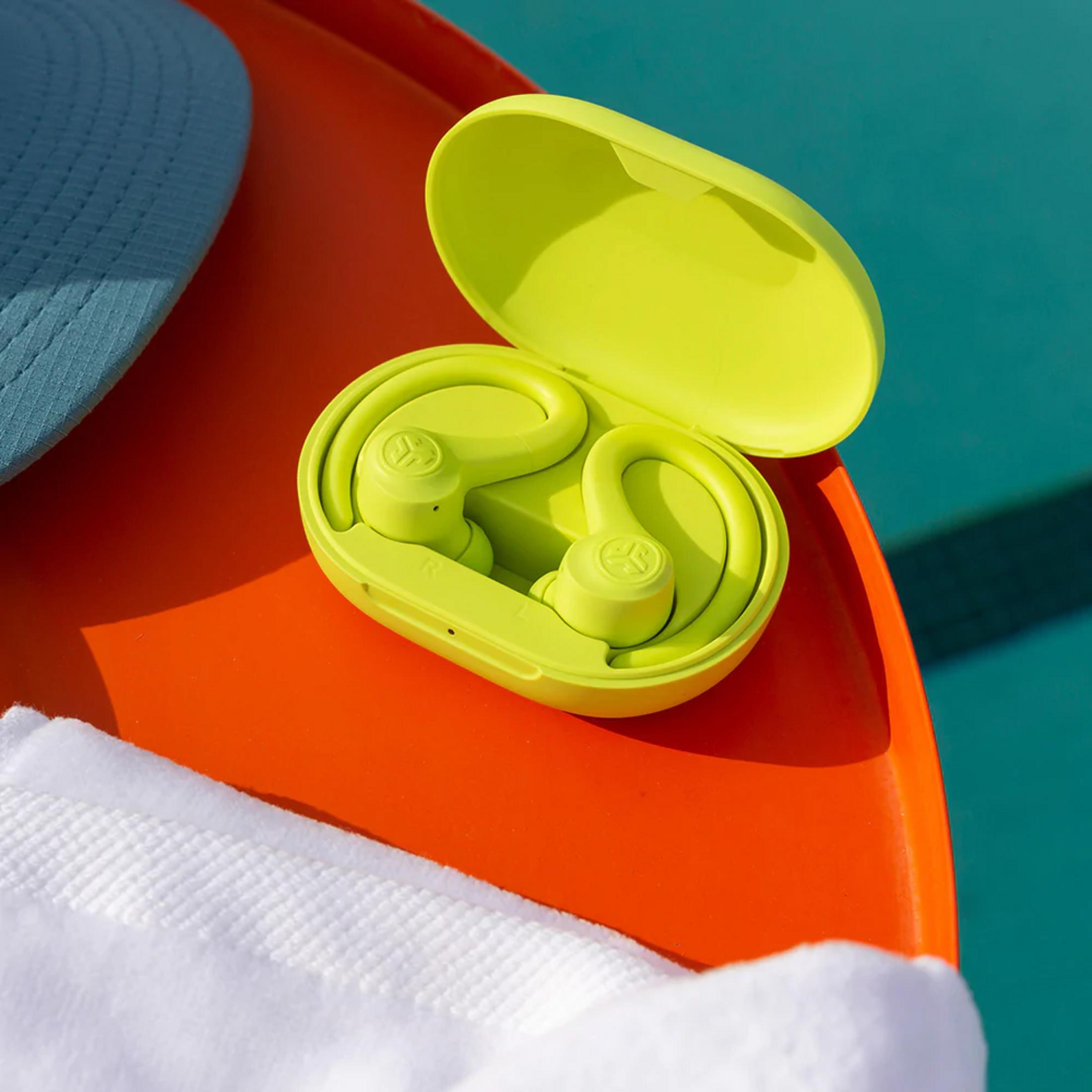 Zielone słuchawki w otwartym etui na pomarańczowej powierzchni obok niebieskiego kapelusza.