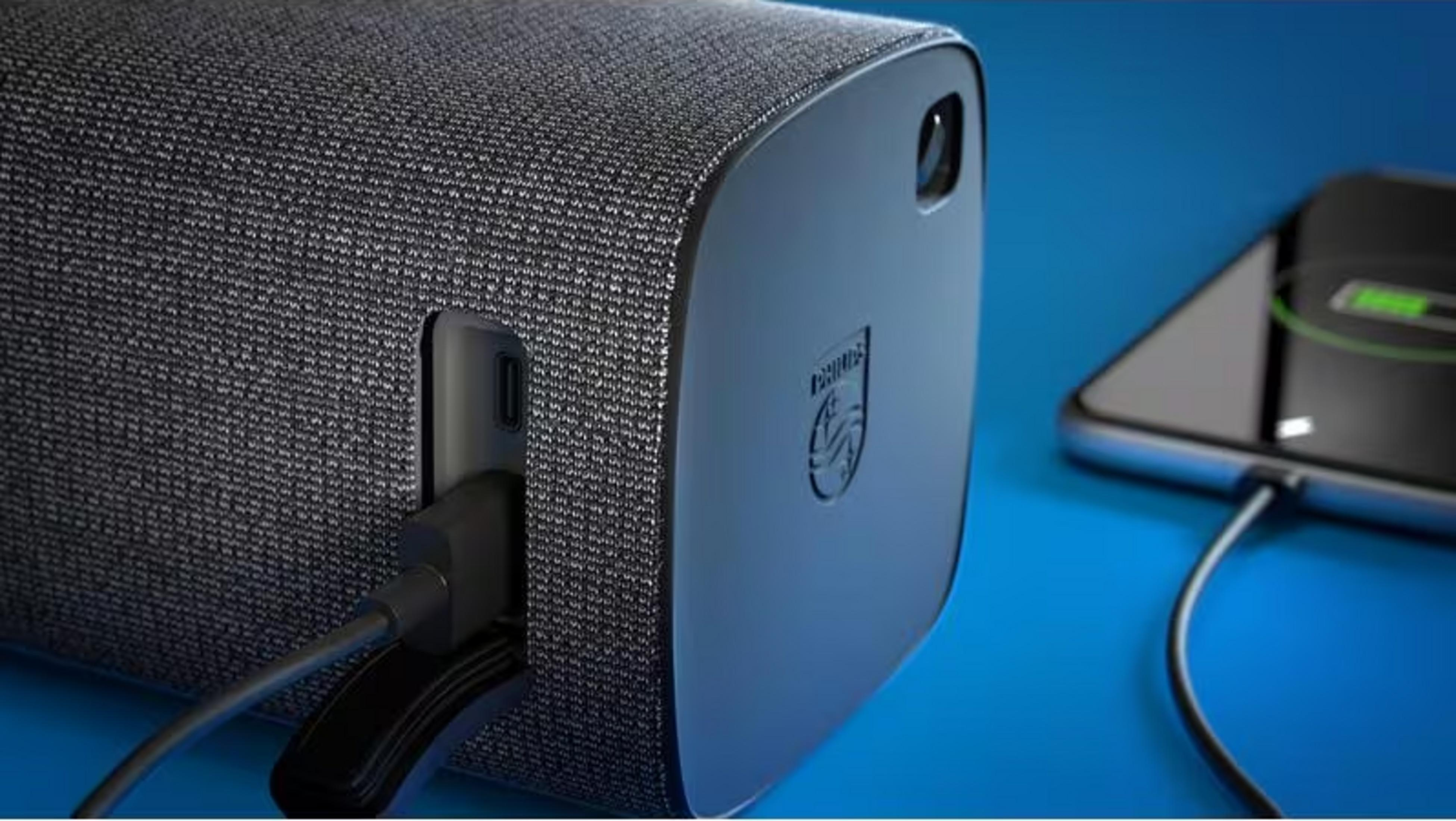 Szara głośnik z portem USB ładuje smartfon na niebieskim tle.