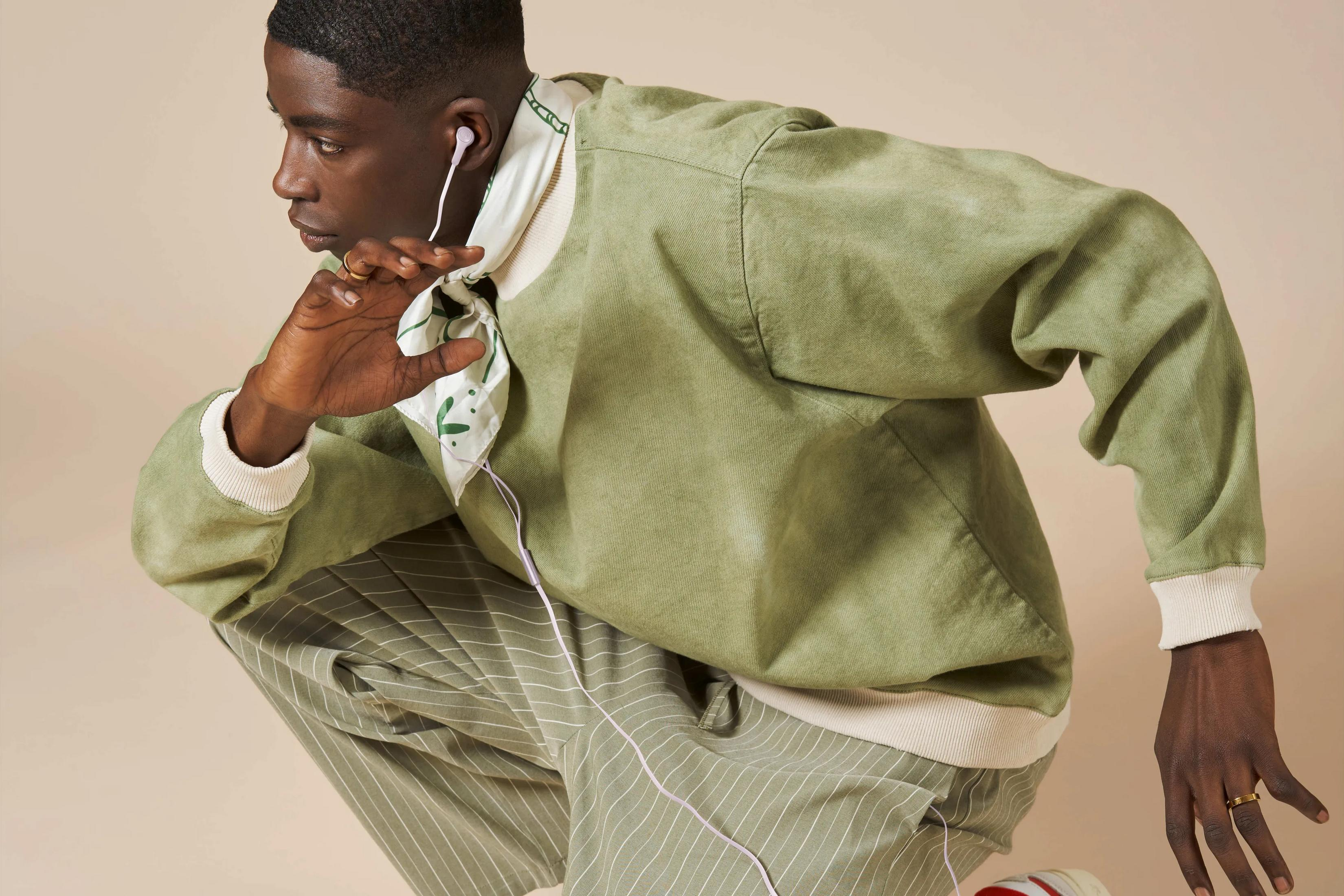 Een man in een groene jas en gestreepte broek met oordopjes.