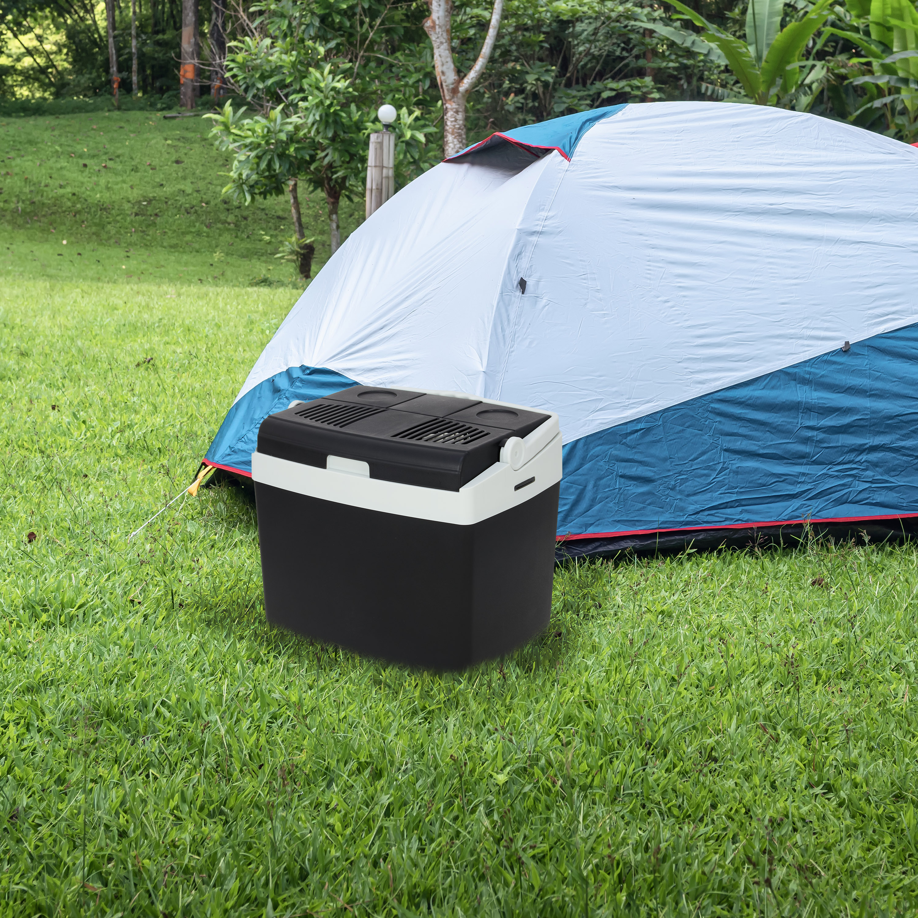 A black cooler sits in front of a blue and white tent on a green grassy field.