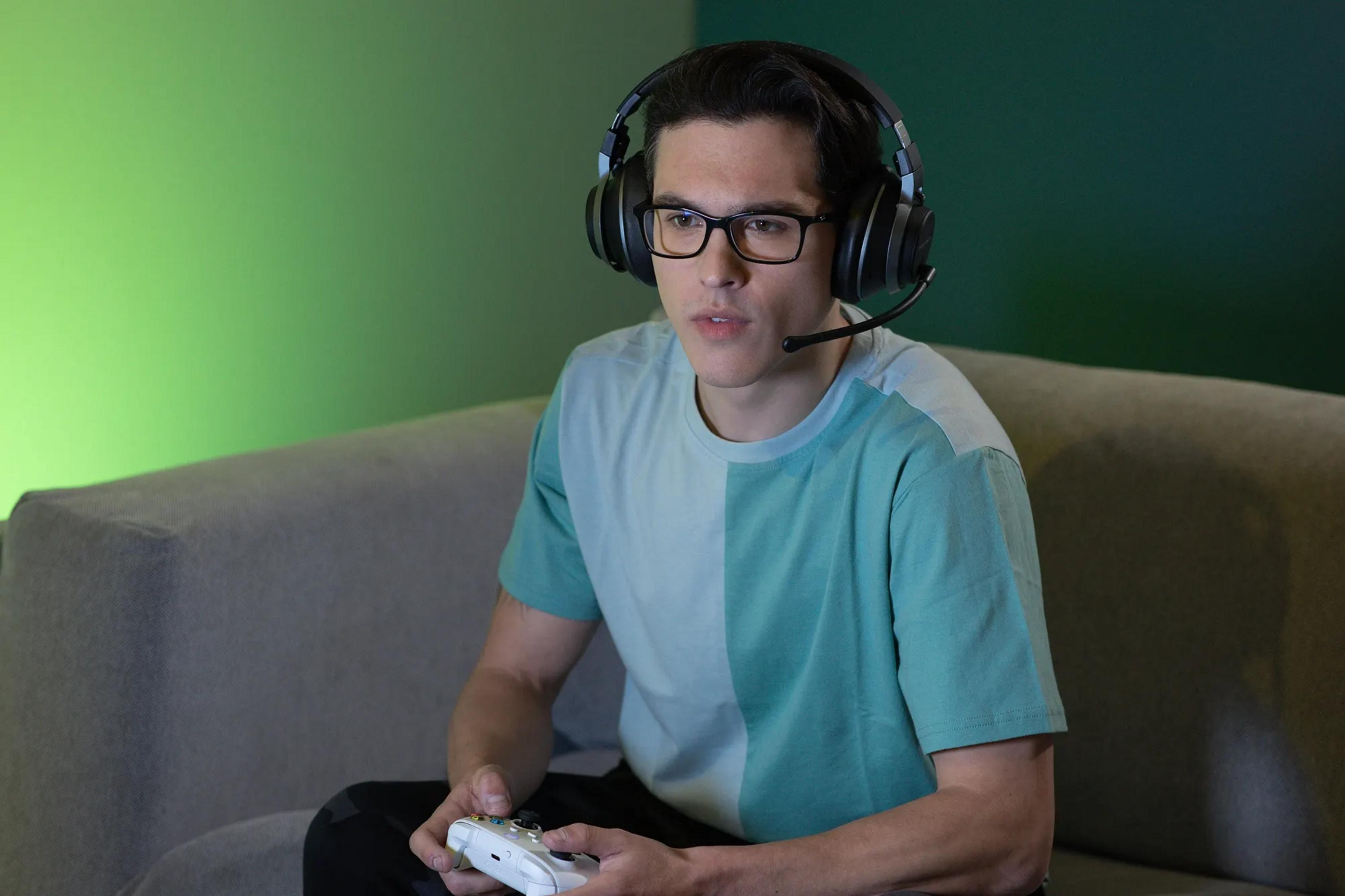 Mężczyzna w okularach i słuchawkach gra w gry wideo na kanapie.