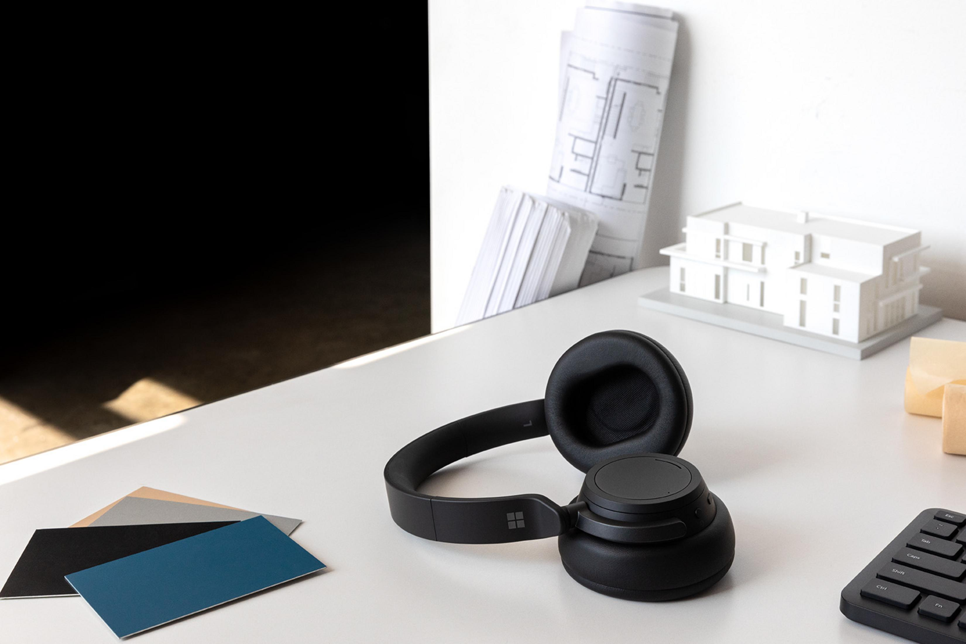Cuffie nere su una scrivania con progetti e modello architettonico.