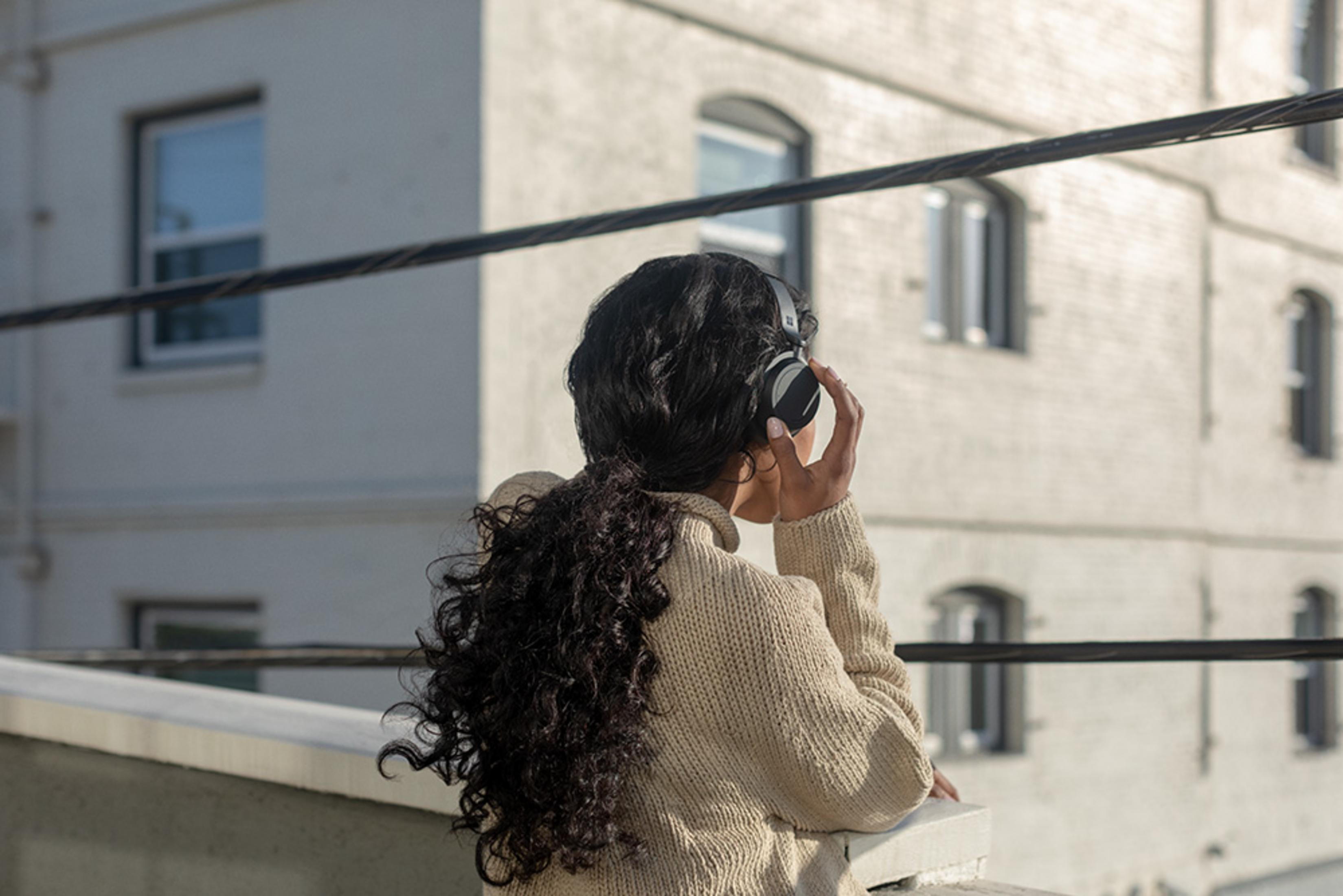 Donna con cuffie in piedi sul balcone davanti a un edificio.
