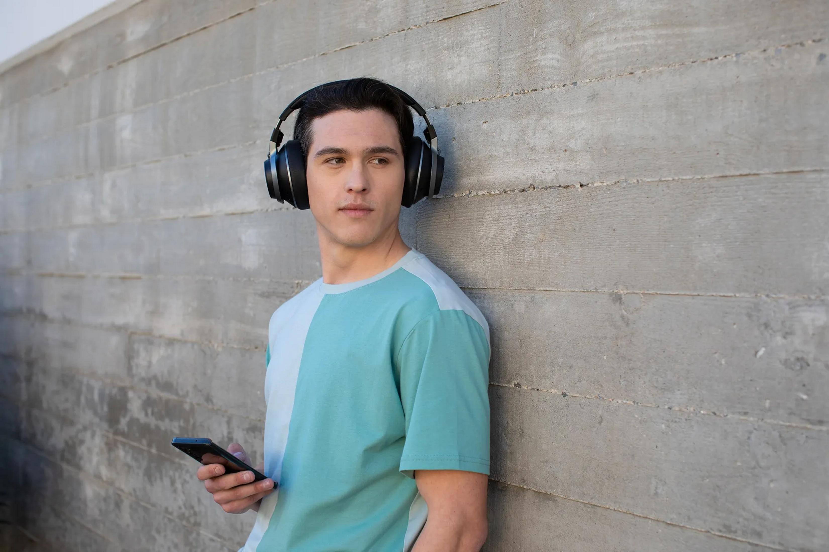 Mężczyzna w słuchawkach i z telefonem opiera się o betonową ścianę.