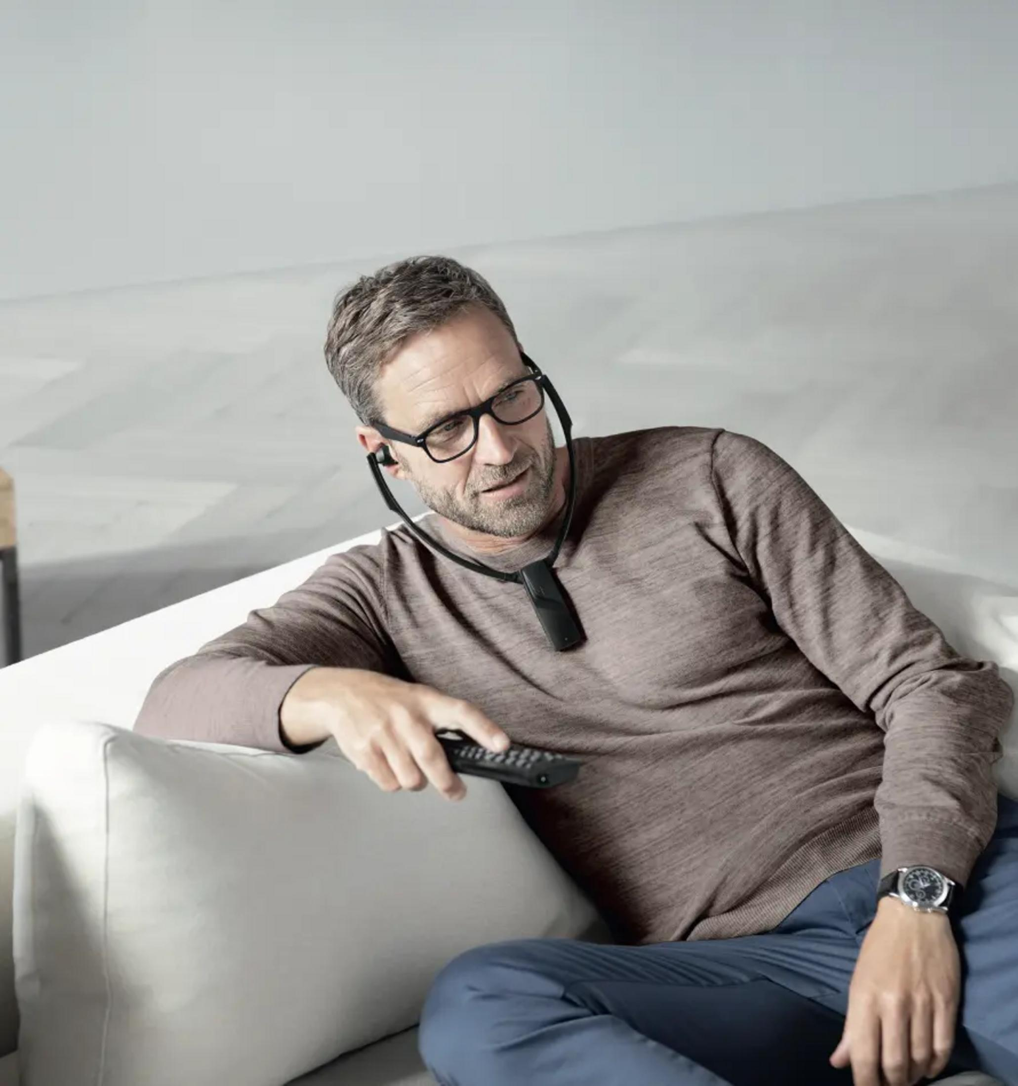 Ein Mann mit Brille sitzt auf einem Sofa und hält eine Fernbedienung.