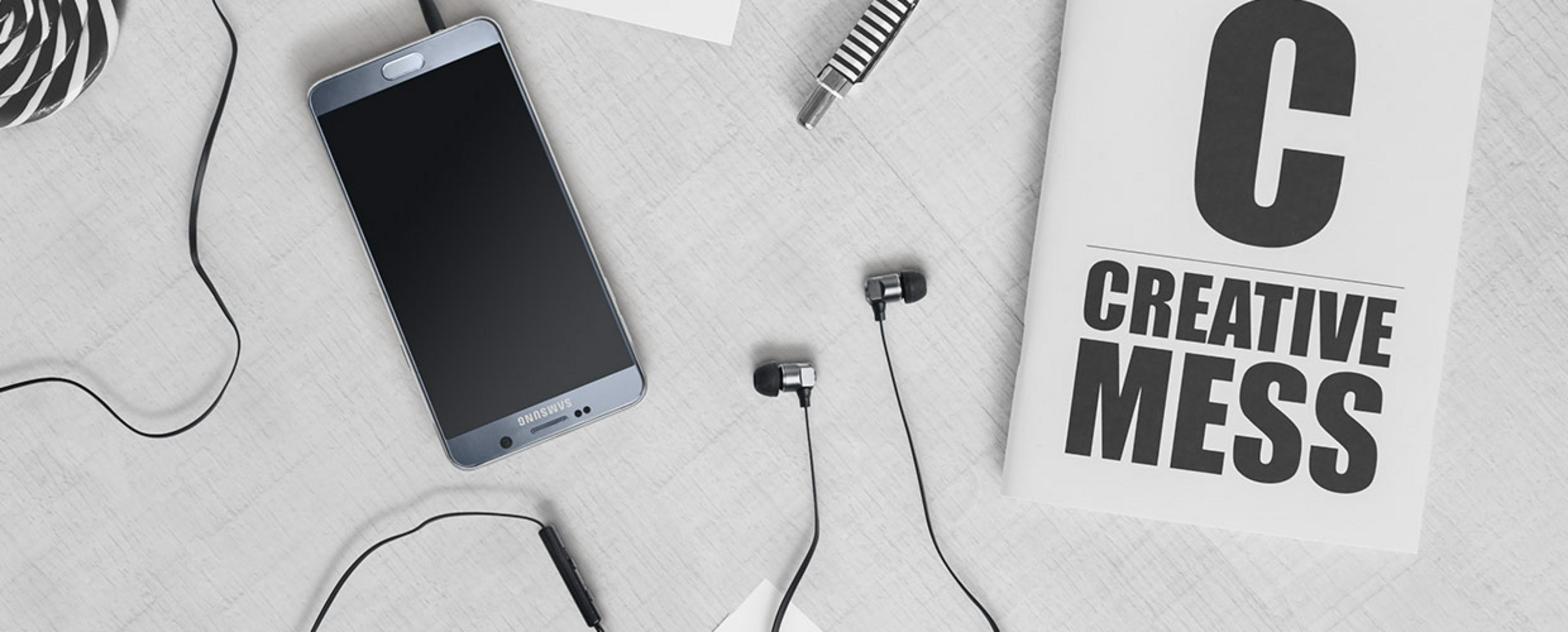 Un teléfono inteligente, auriculares, un bolígrafo y un libro que dice "CREATIVE MESS" sobre una mesa.