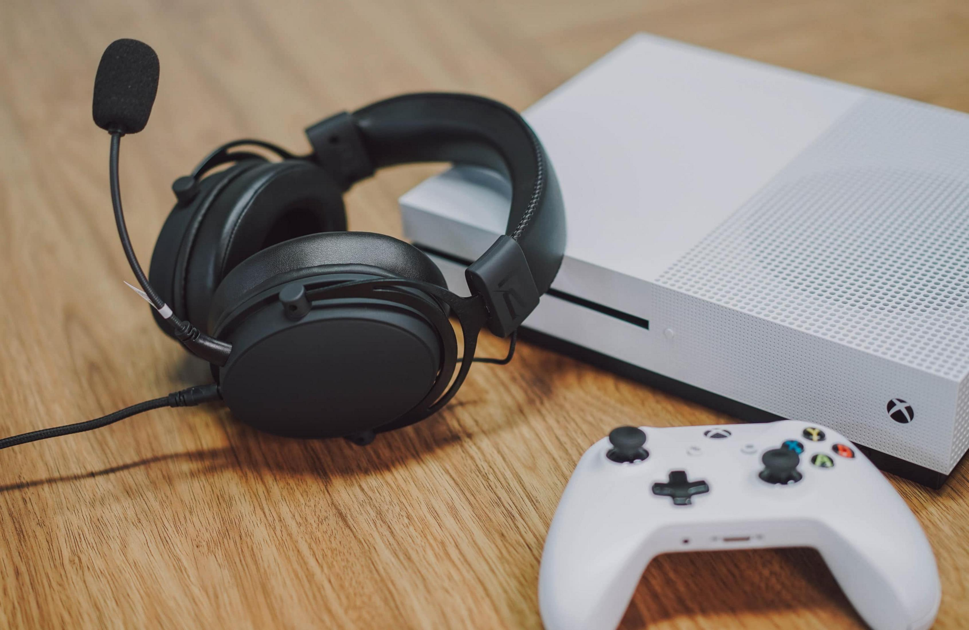 Schwarzes Gaming-Headset, weiße Xbox-Konsole und Controller auf Holzoberfläche.