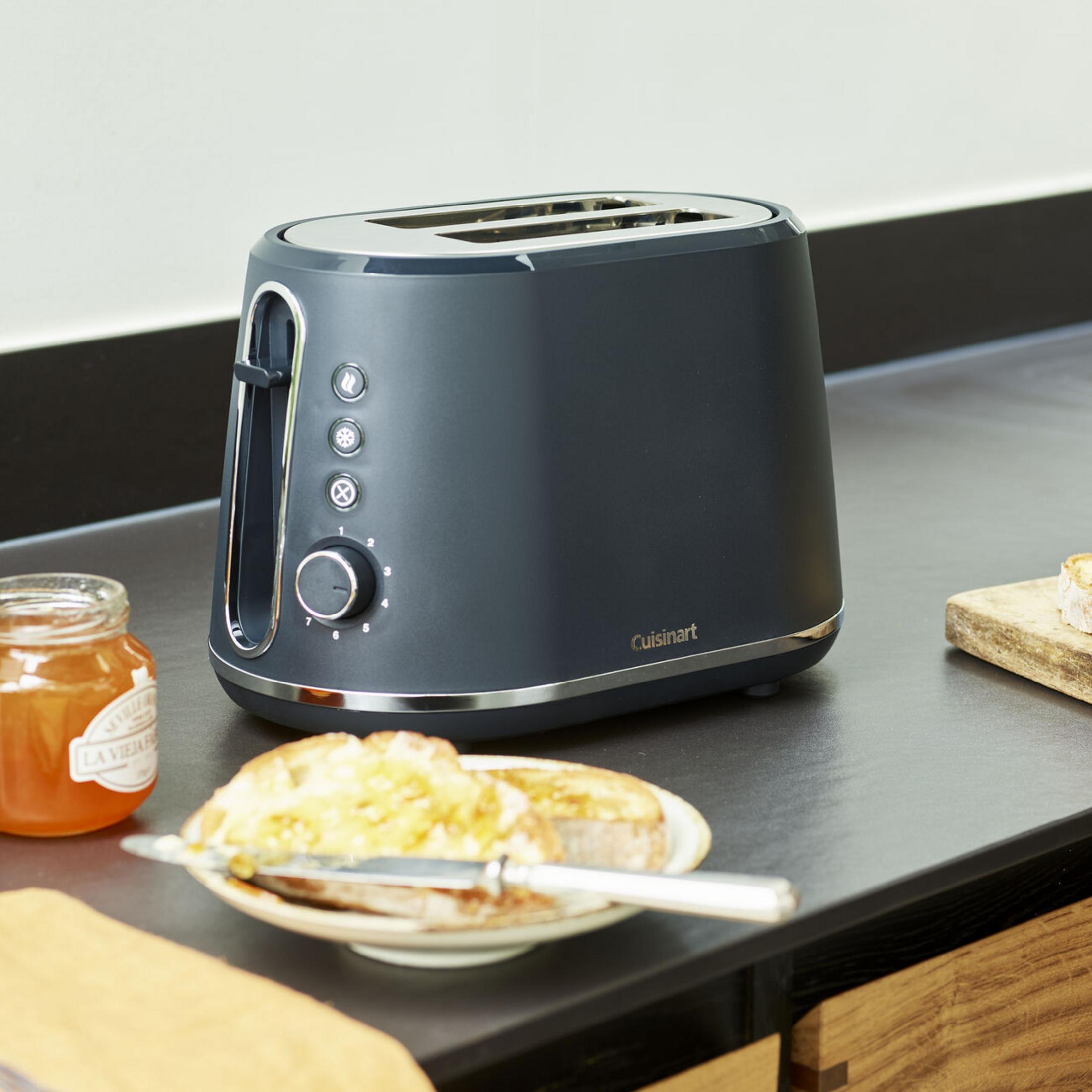 Een donkere broodrooster staat op een aanrecht naast een pot jam en toast.
