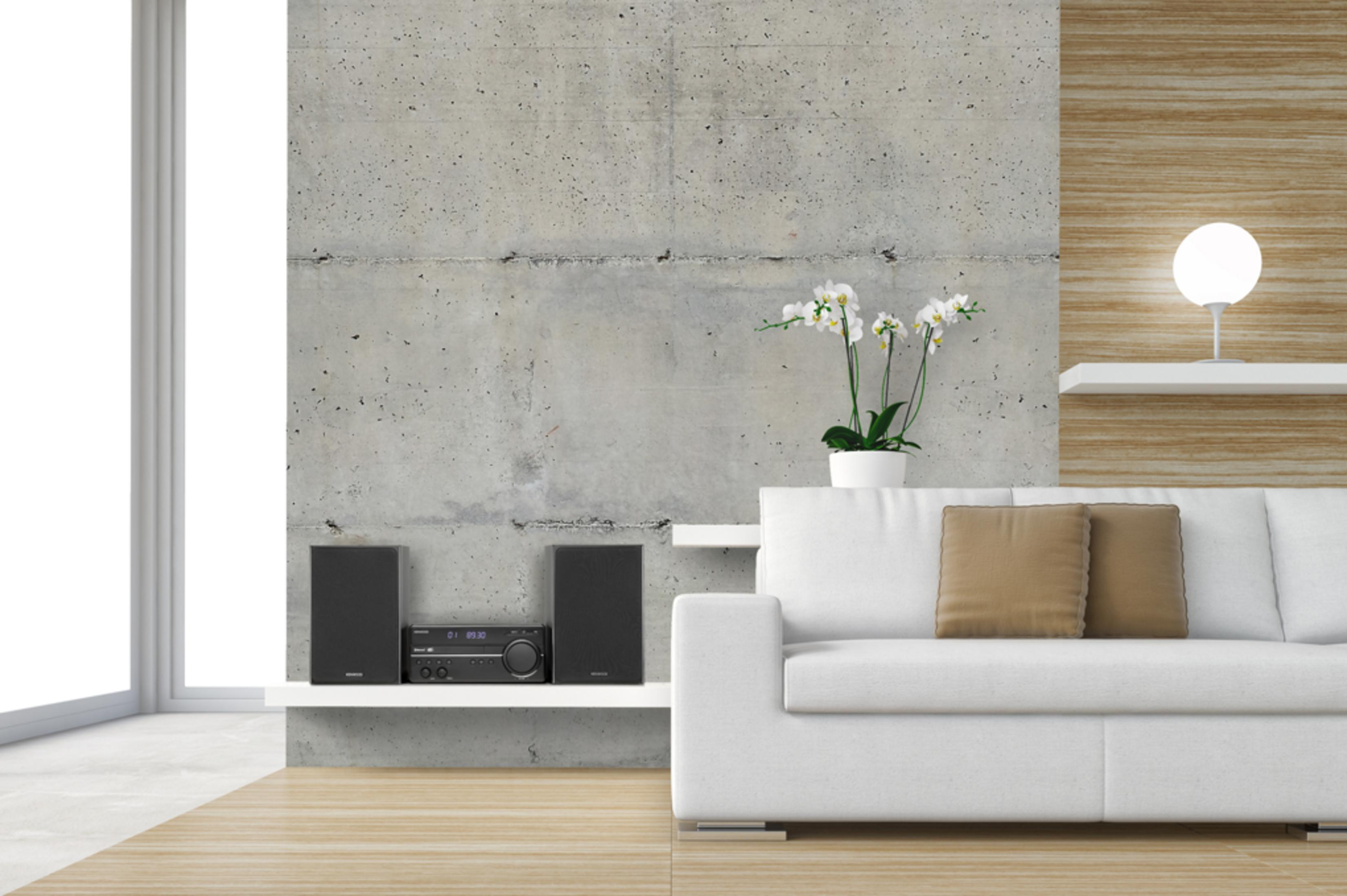 Una sala de estar moderna con pared de concreto, sofá, flores y equipo de sonido.
