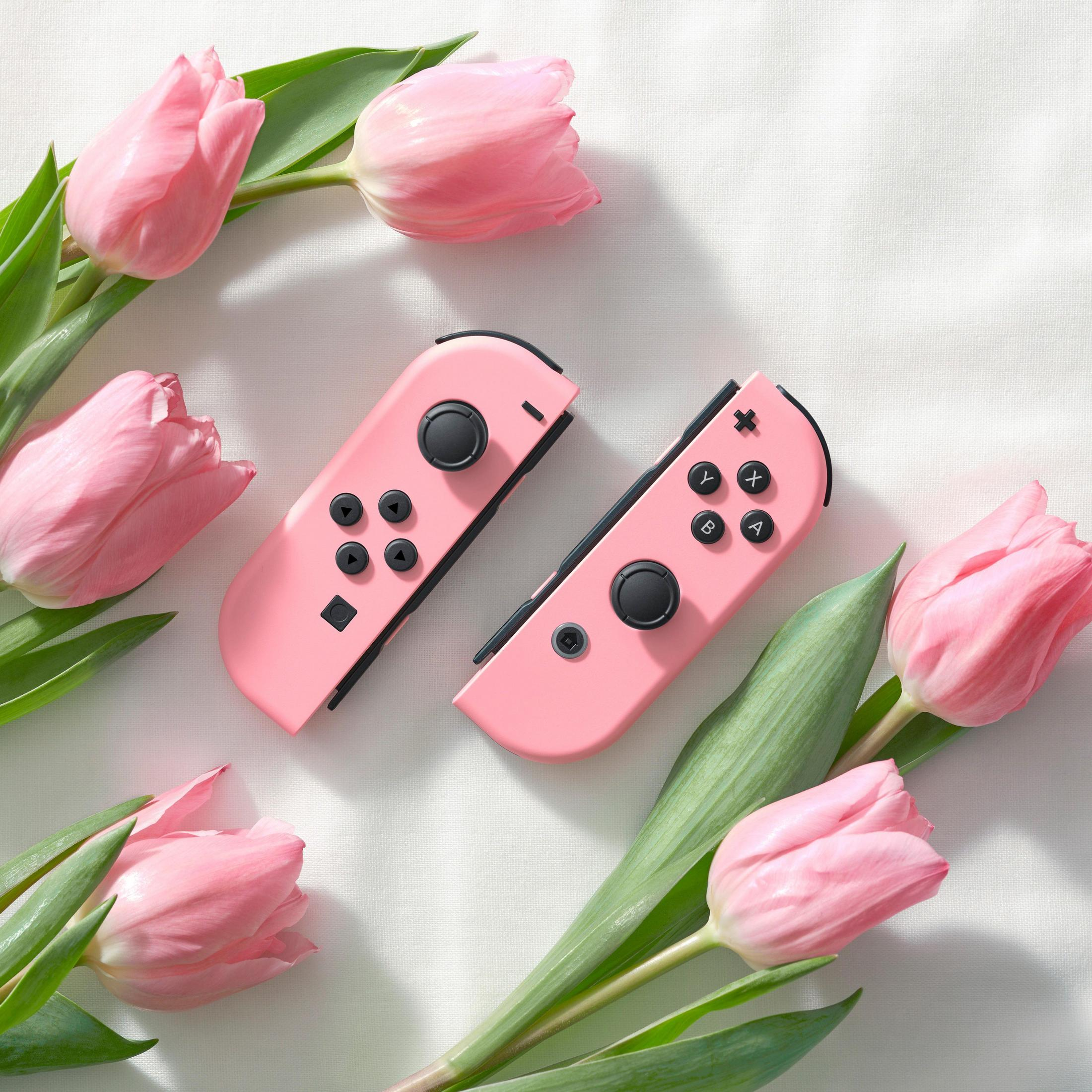 Dwa różowe kontrolery Nintendo Switch Joy-Con leżą wśród różowych tulipanów.