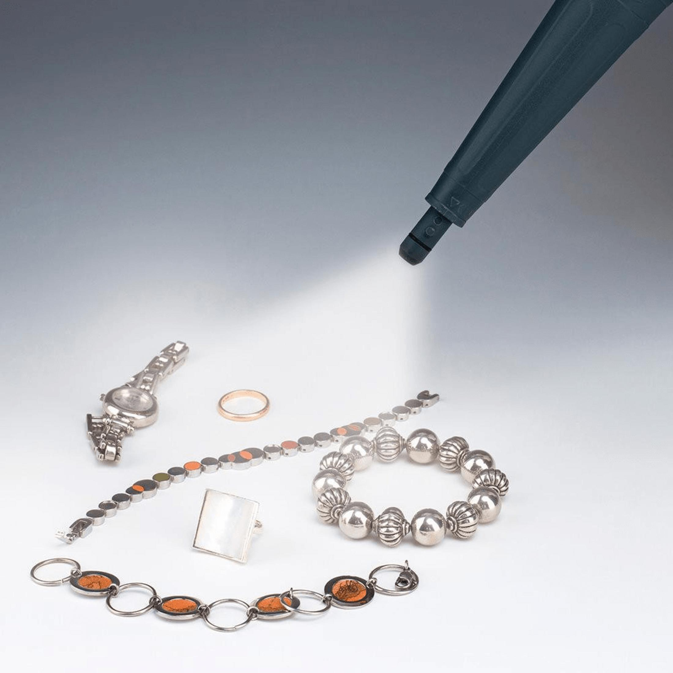 Des bijoux, dont une montre et des bracelets, sont éclairés par un faisceau lumineux.