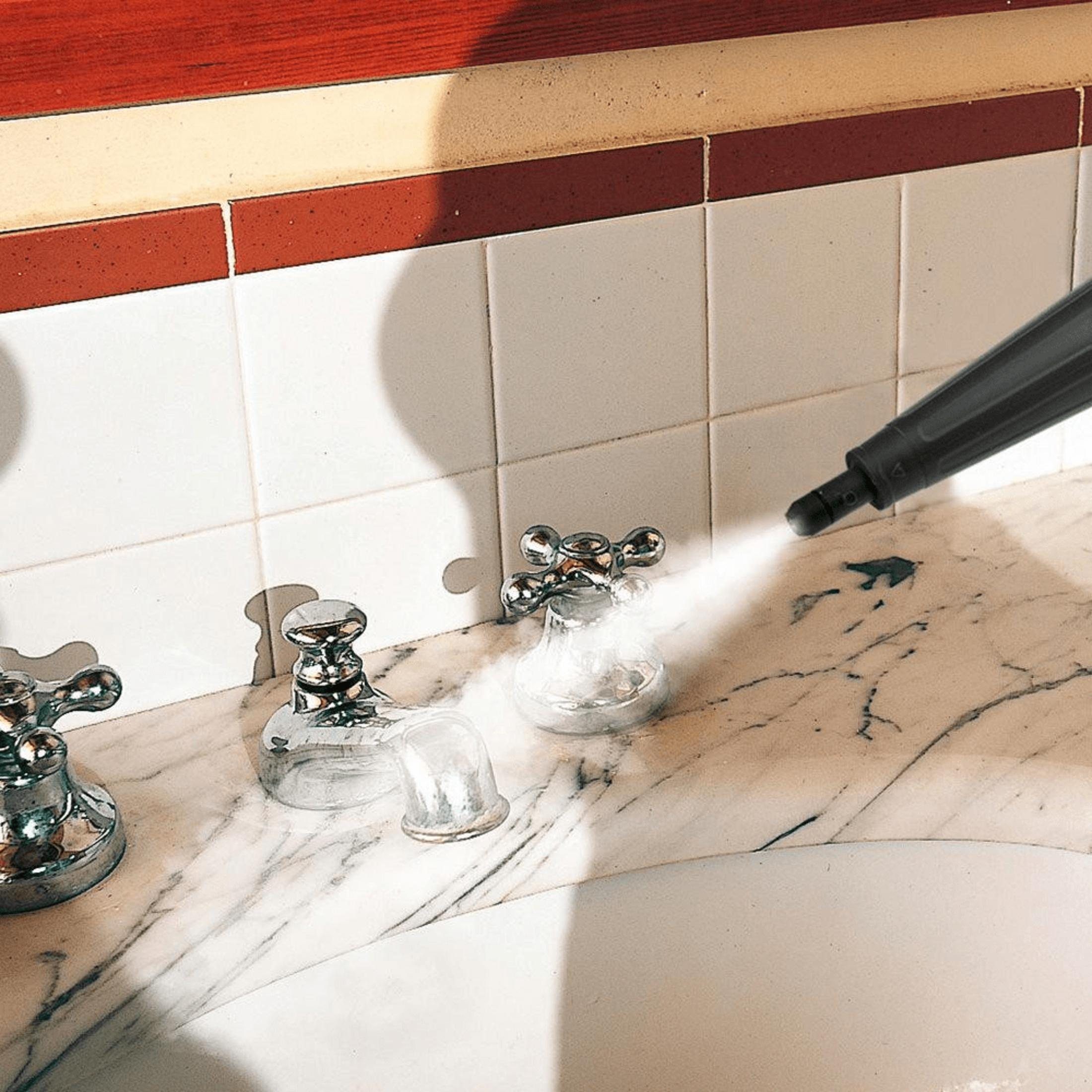 Nettoyeur vapeur désinfectant des robinets sur vanité en marbre avec carrelage blanc.