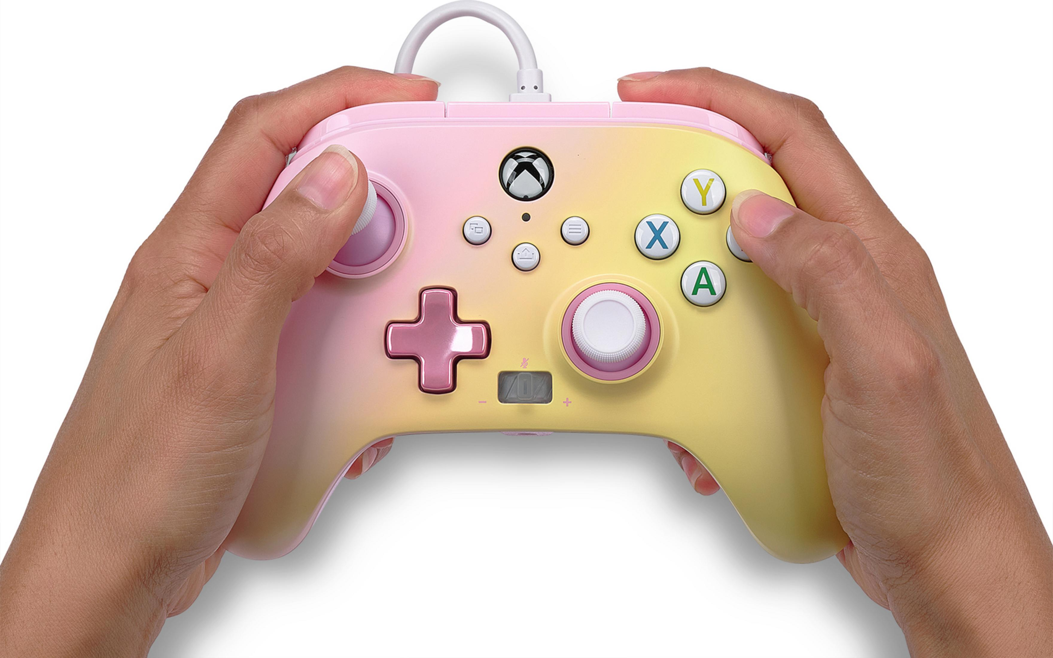 Mani che tengono un controller Xbox sfumato rosa pastello e giallo.
