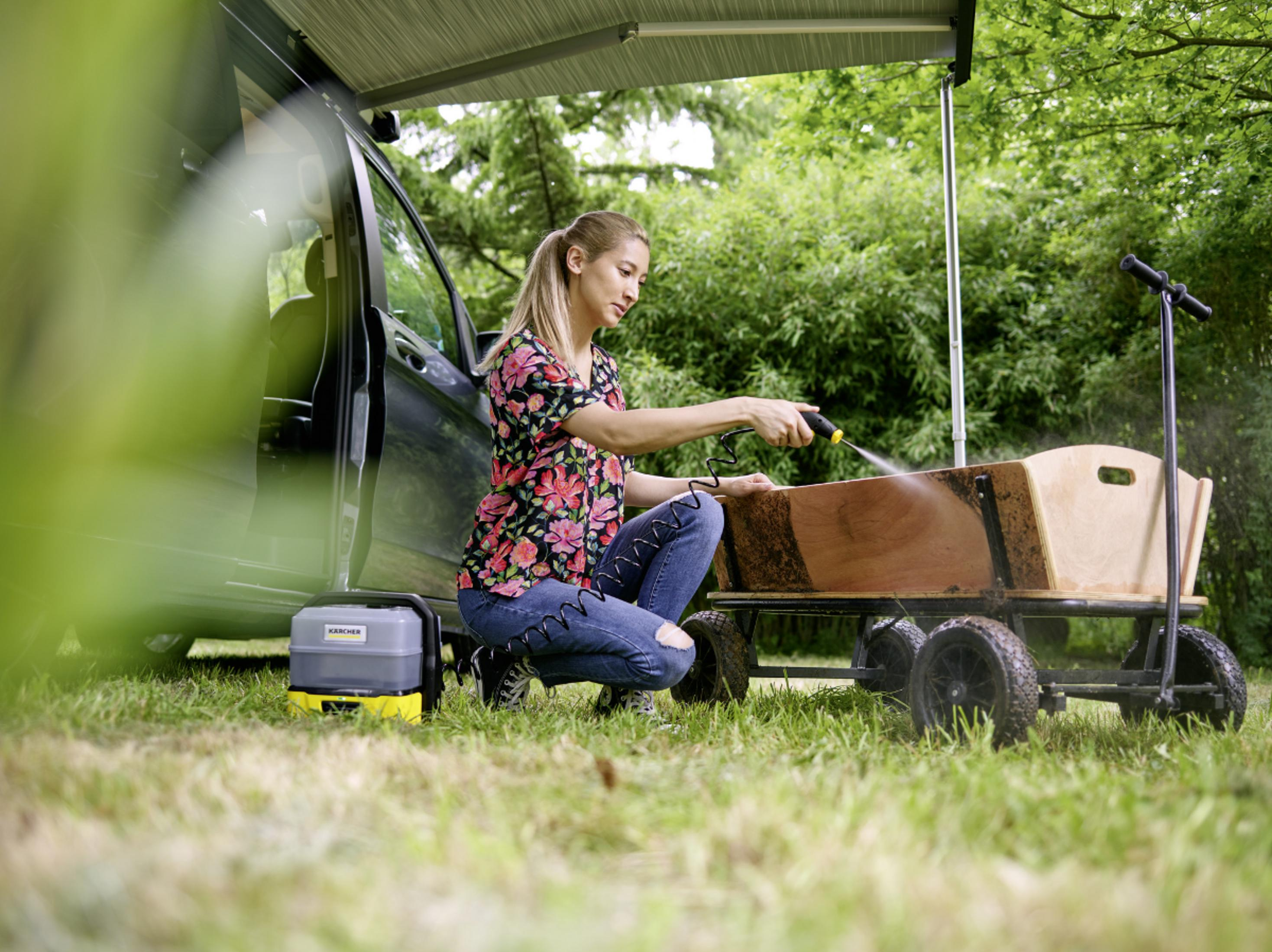 Donna pulisce carretto in legno con idropulitrice vicino auto all'aperto.