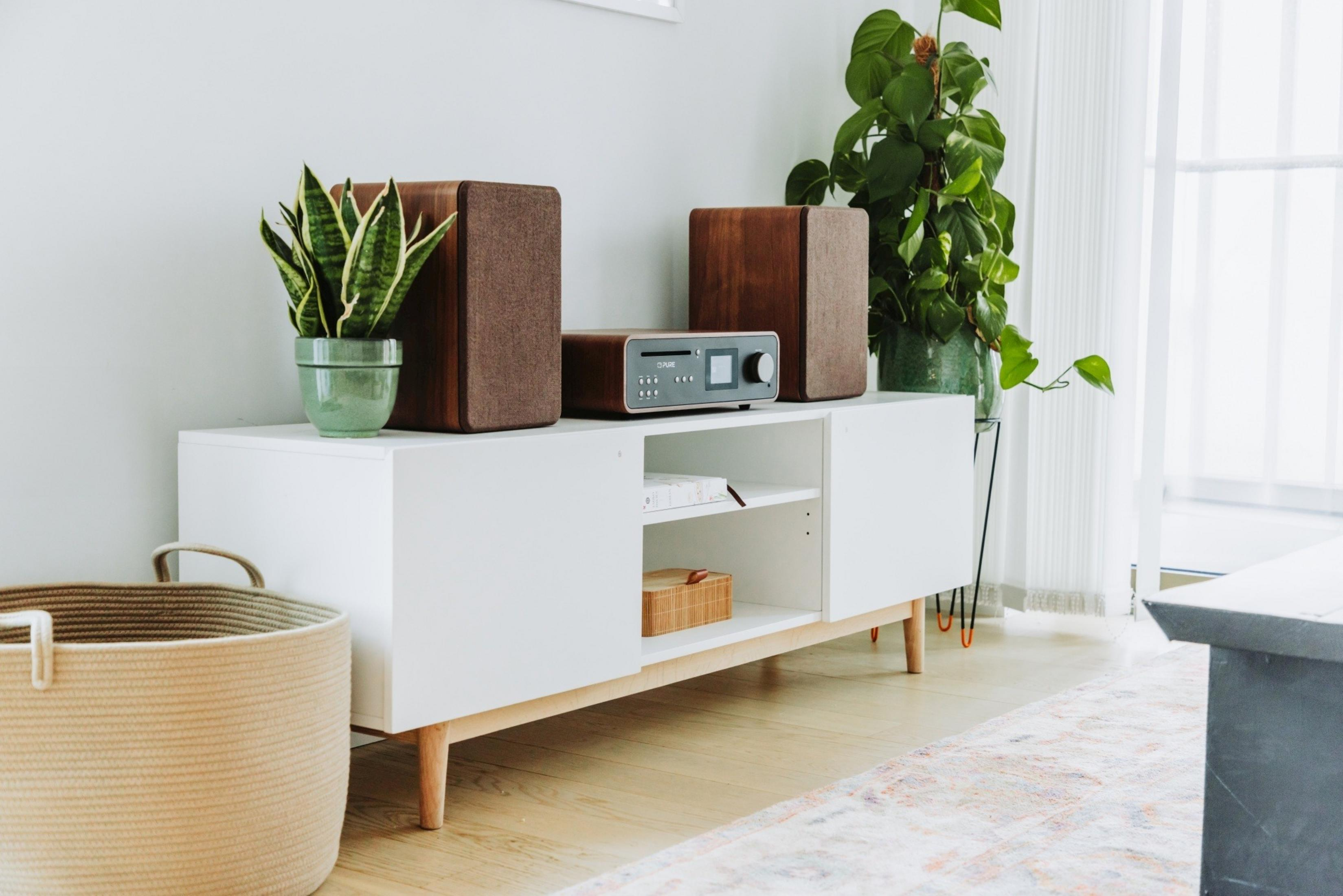 Ein weißes Sideboard mit Lautsprechern, Pflanzen und einem Korb.