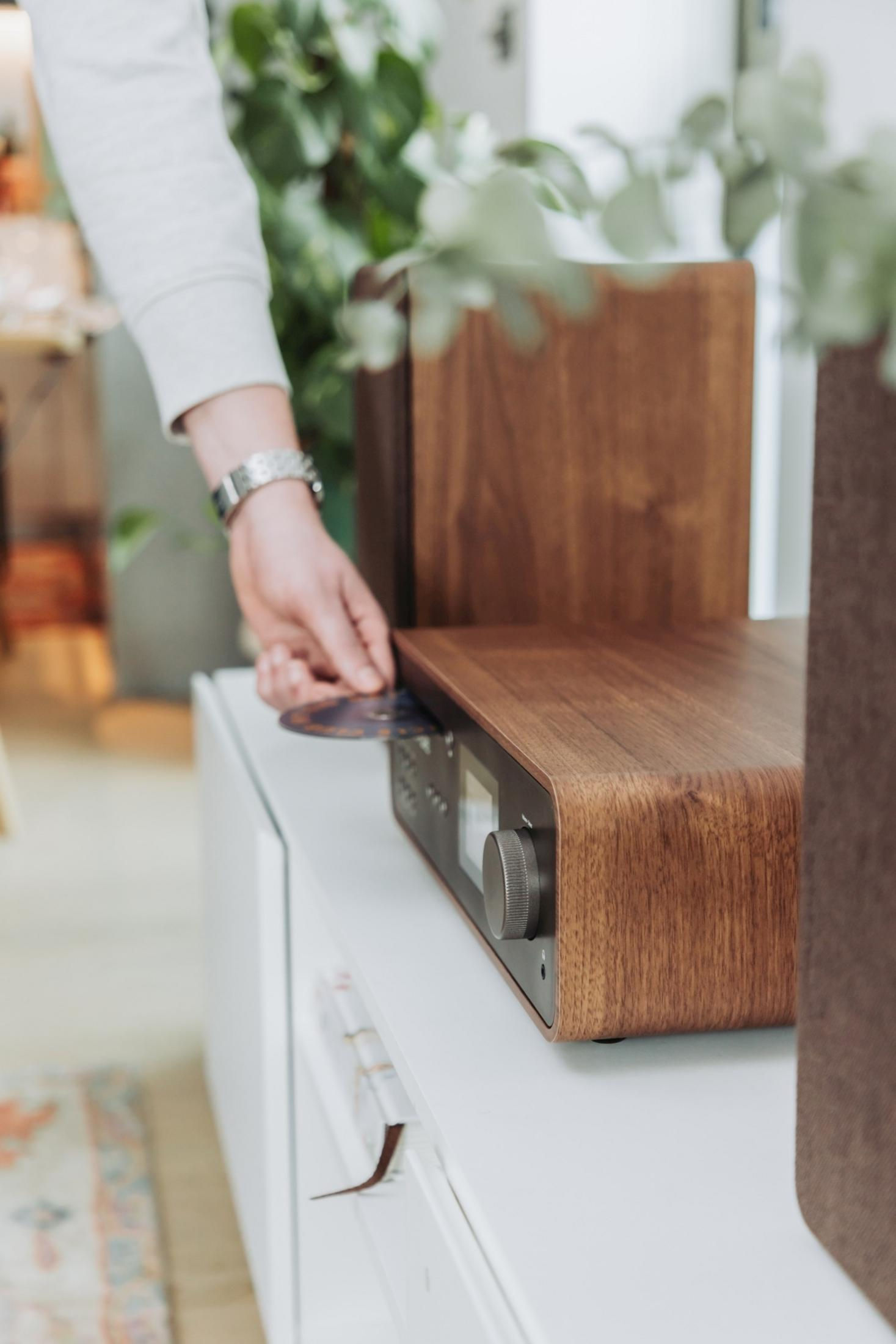 Eine Hand schiebt eine CD in ein Holzgehäuse-Radio auf einem weißen Schrank.