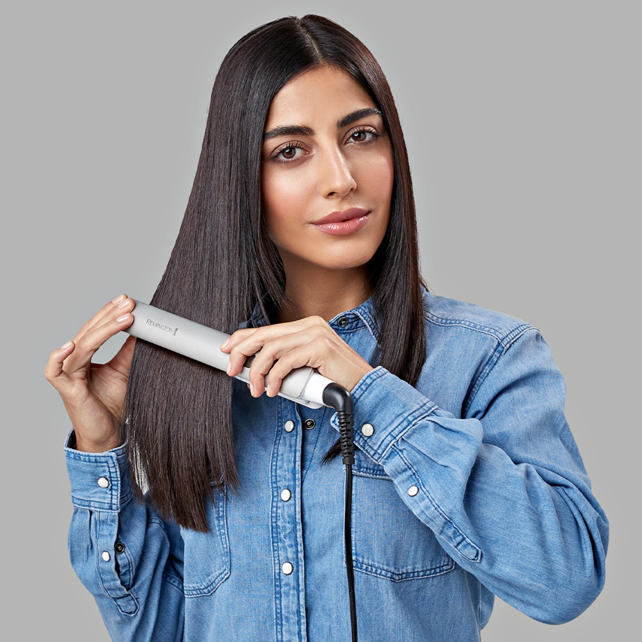 Kobieta z długimi, ciemnymi włosami prostuje je prostownicą Remington.