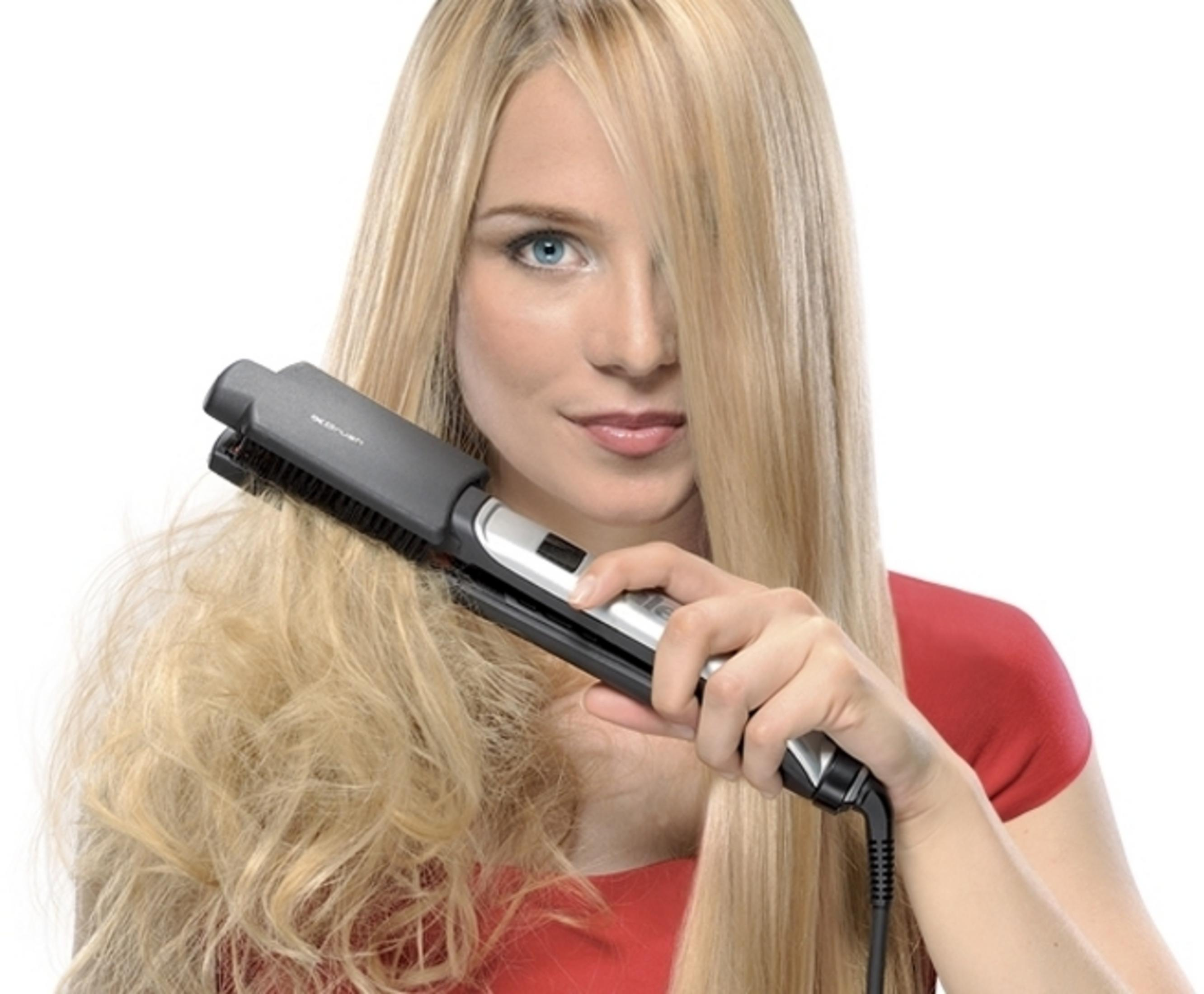 Una donna bionda in maglietta rossa si liscia i capelli con una spazzola lisciante nera e argento.