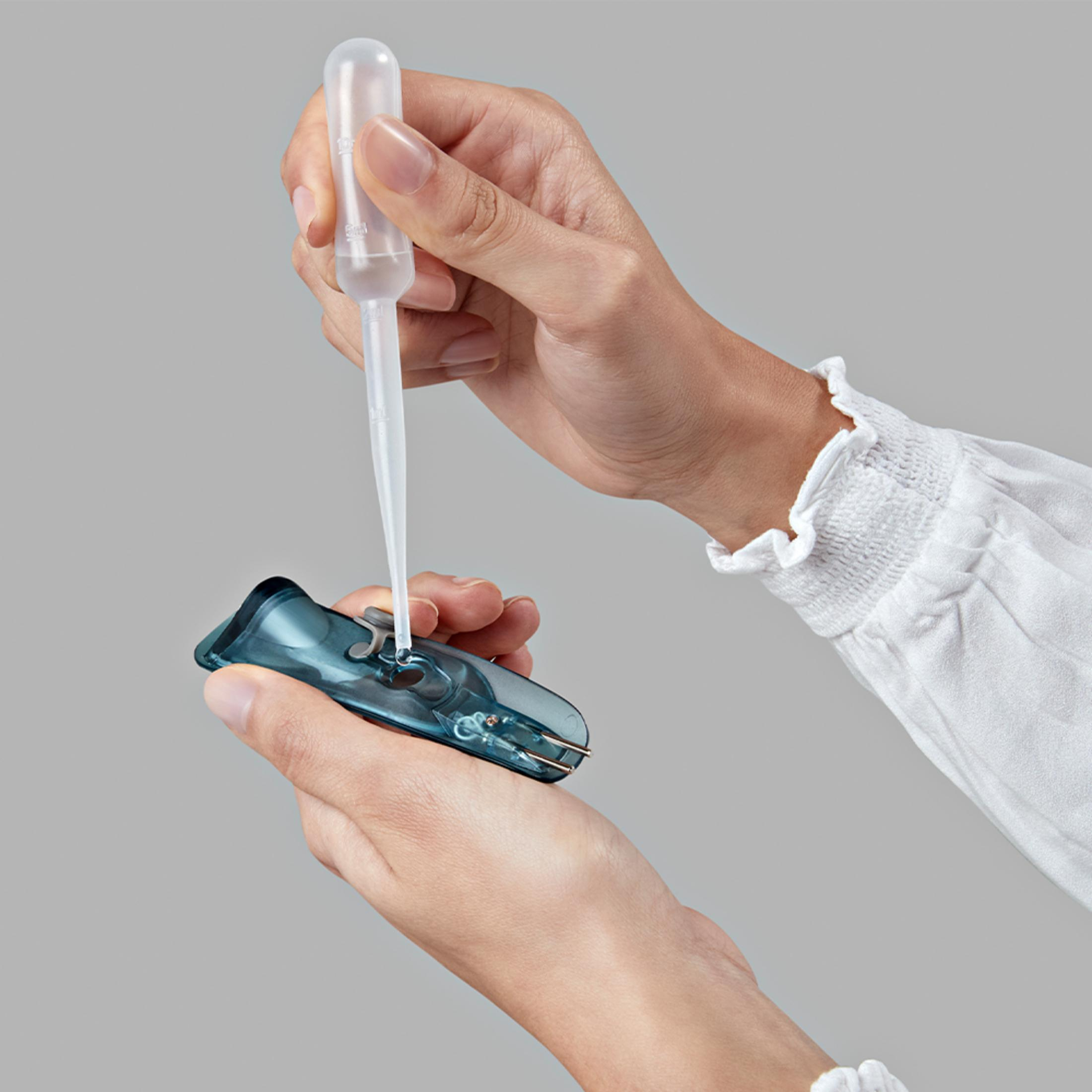 Mani usano contagocce per gocciolare liquido in dispositivo blu.