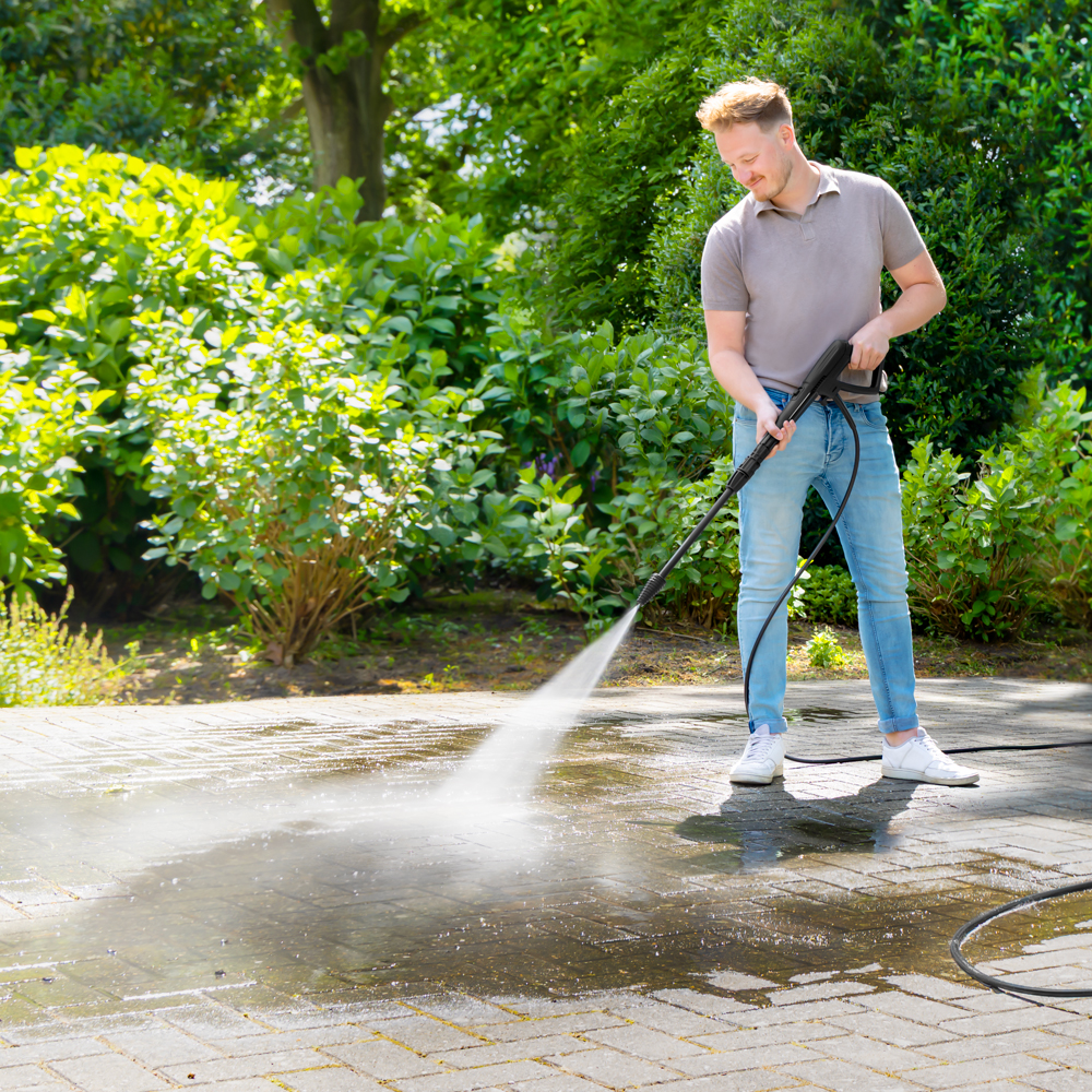Man reinigt bestrating met hogedrukreiniger in een tuin.