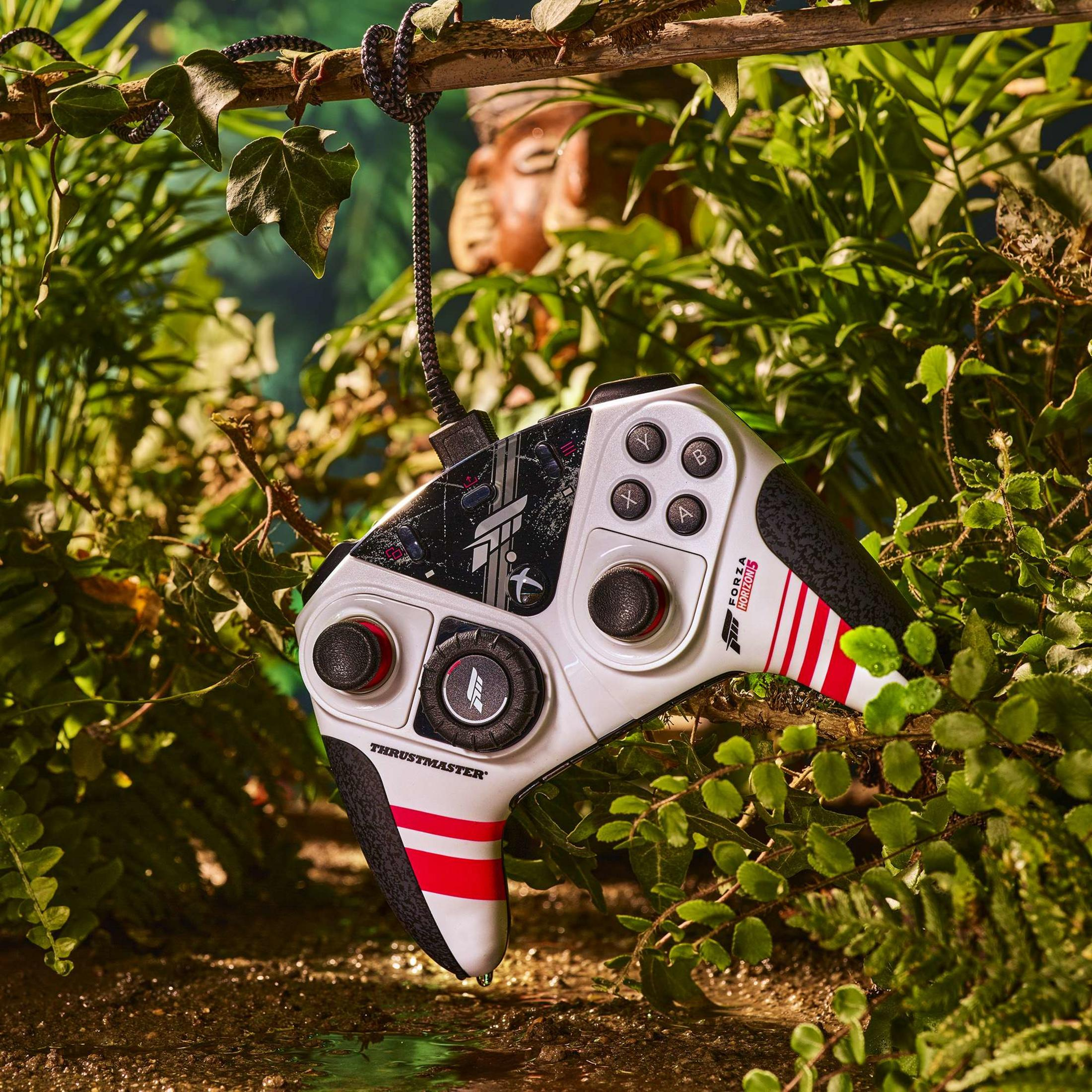 Biały kontroler do gier z czerwono-czarnymi akcentami wisi na gałęzi w scenerii dżungli.