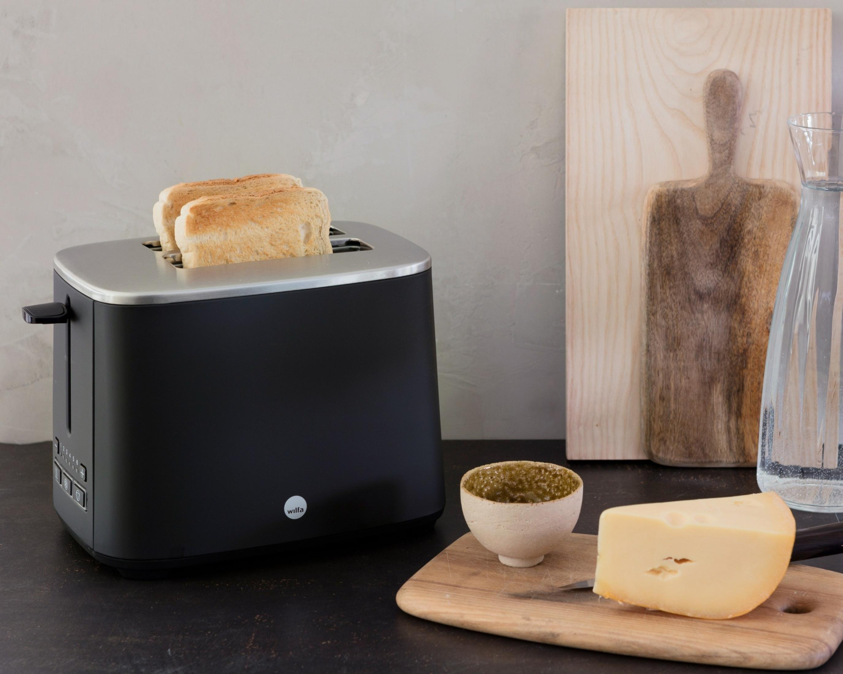Ein schwarzer Toaster mit zwei Scheiben Toast, daneben Käse und eine Schale.