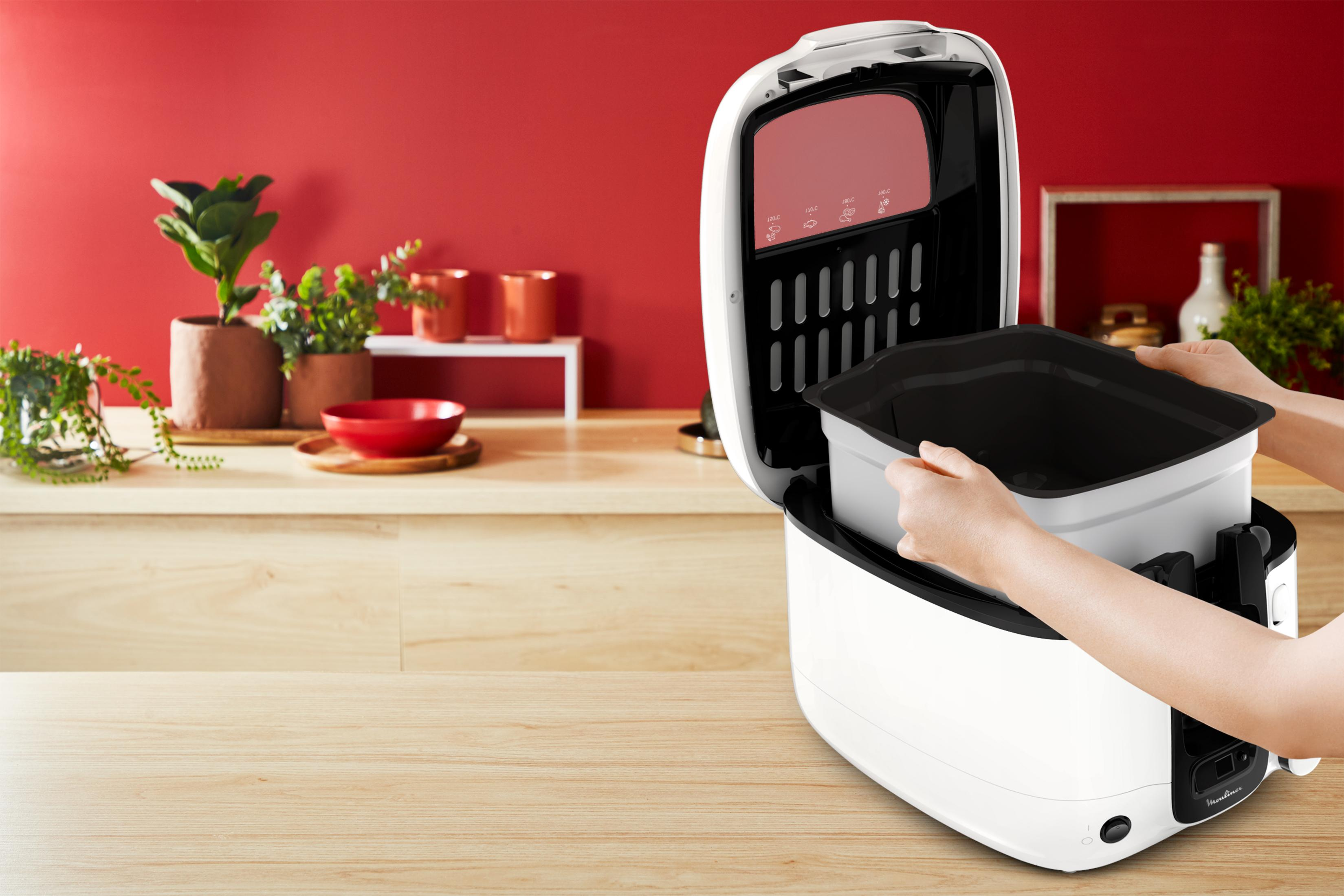 Osoba wkłada kosz do wnętrza białej frytownicy beztłuszczowej.