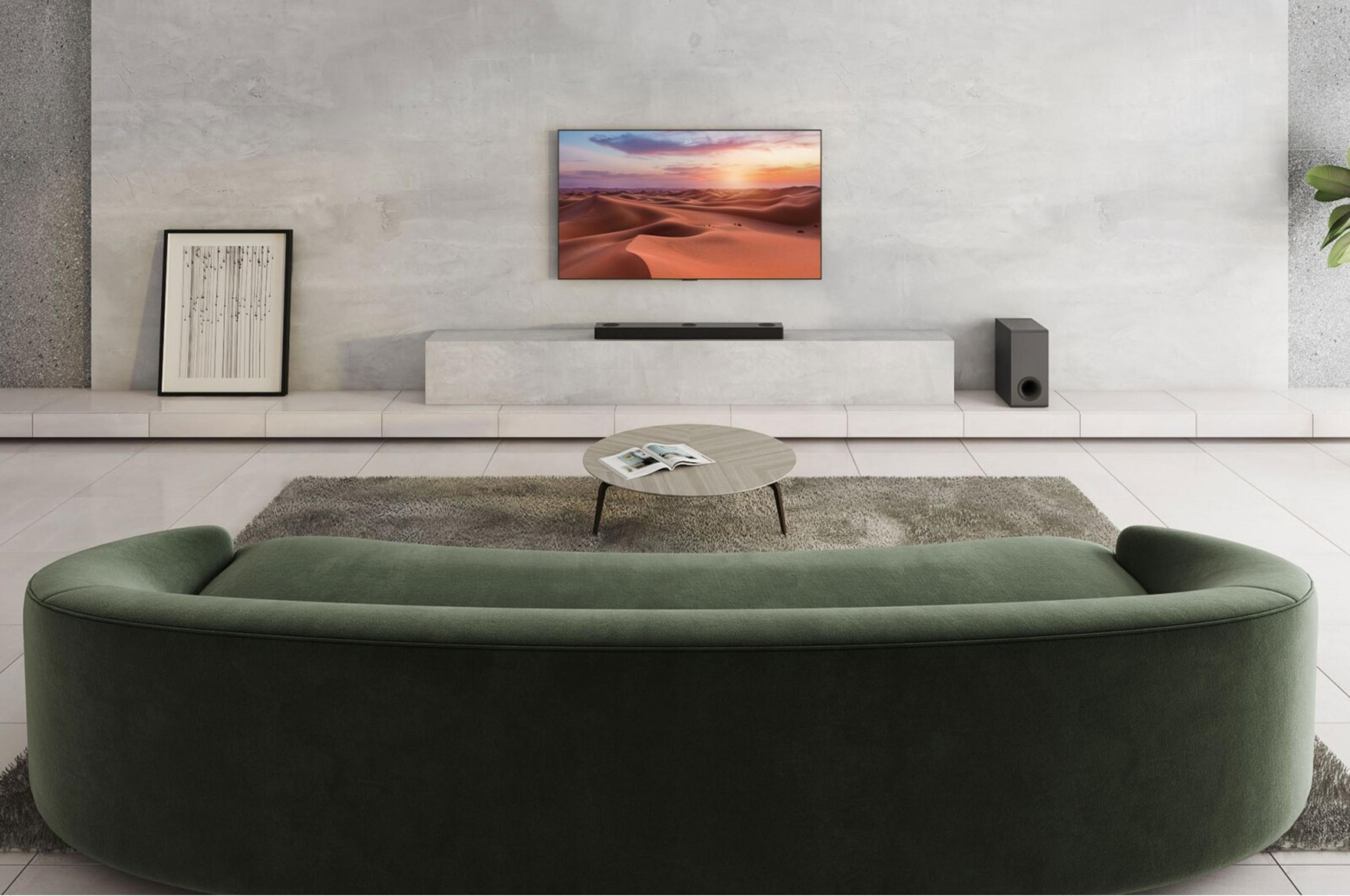 Ein grünes Sofa steht vor einem Couchtisch auf einem Teppich. Eine Leinwand zeigt eine Wüstenlandschaft.