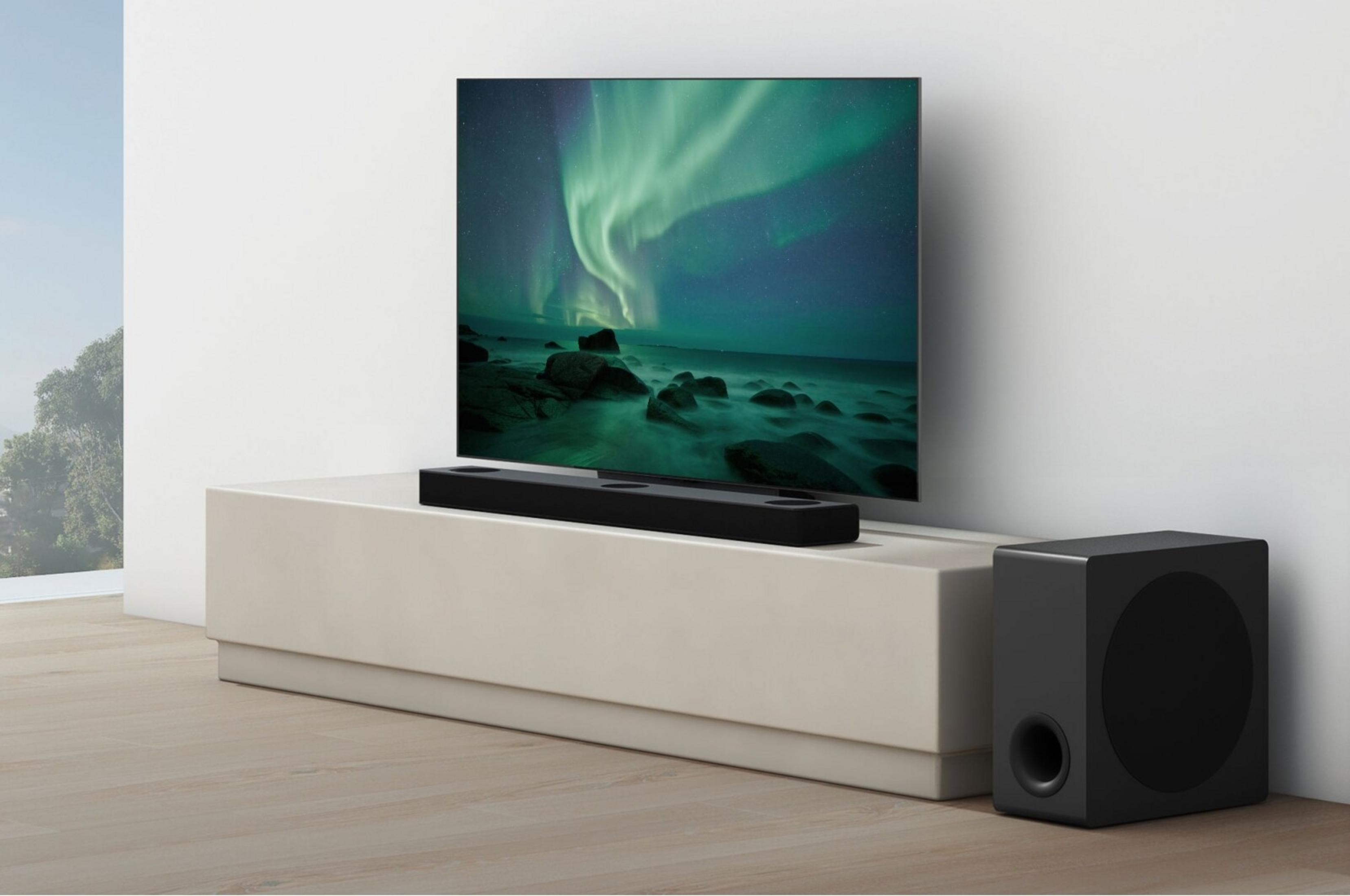 Ein schwarzer Subwoofer steht neben einem TV-Möbel mit Soundbar und Fernseher.