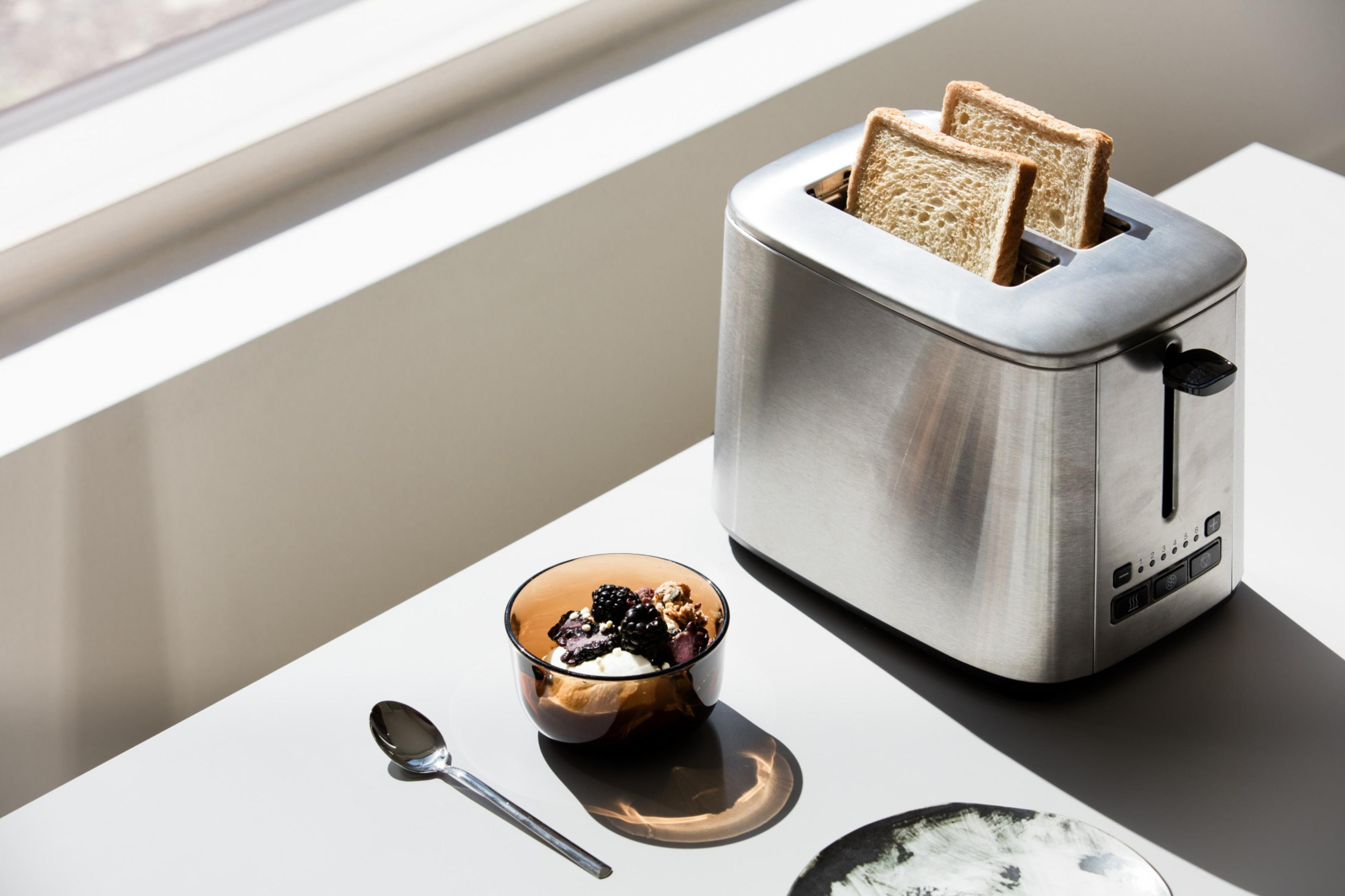 Ein Toaster mit zwei Scheiben Toast, daneben eine Schale mit Joghurt und Beeren.