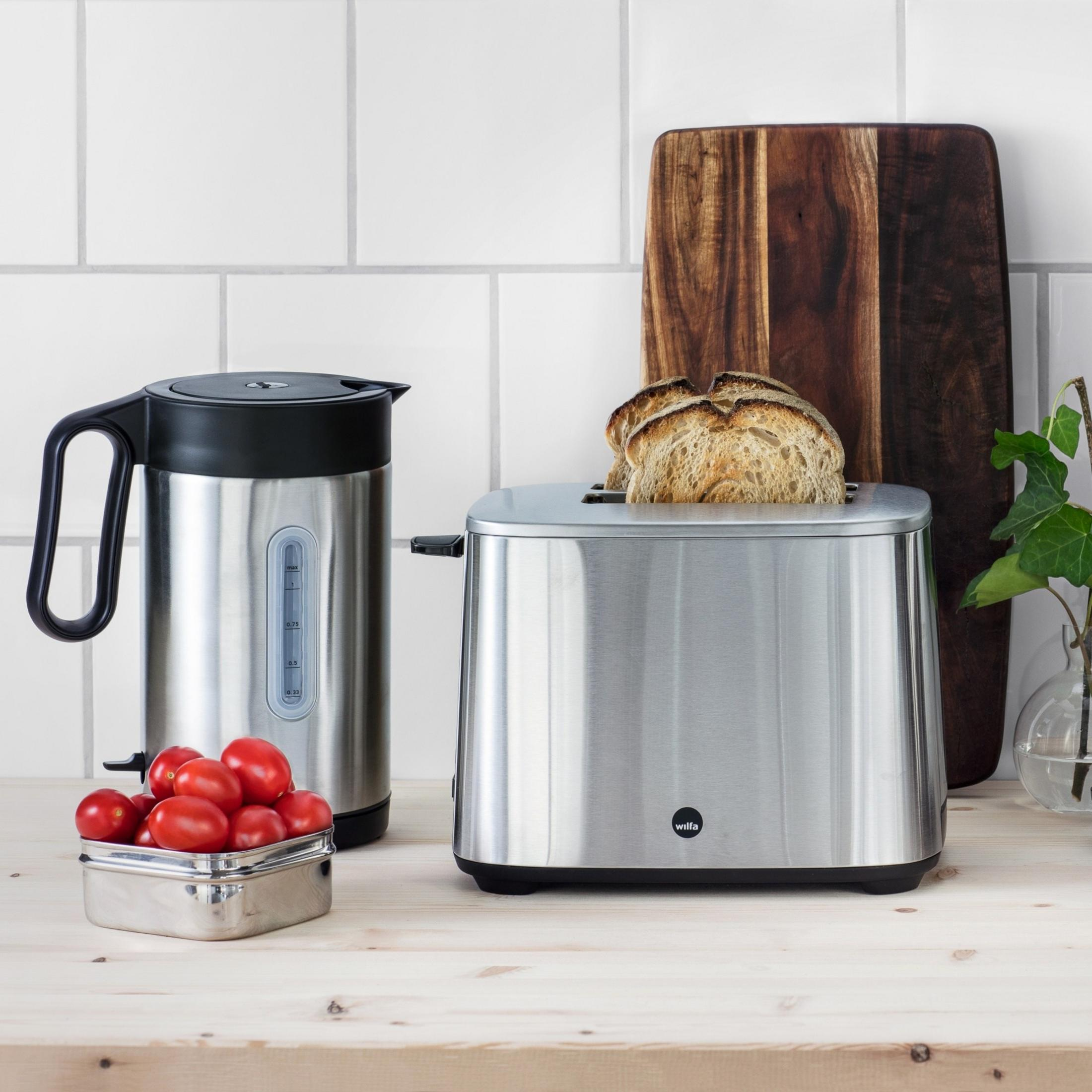 Ein silberner Toaster mit Brot, daneben ein Wasserkocher und Tomaten.