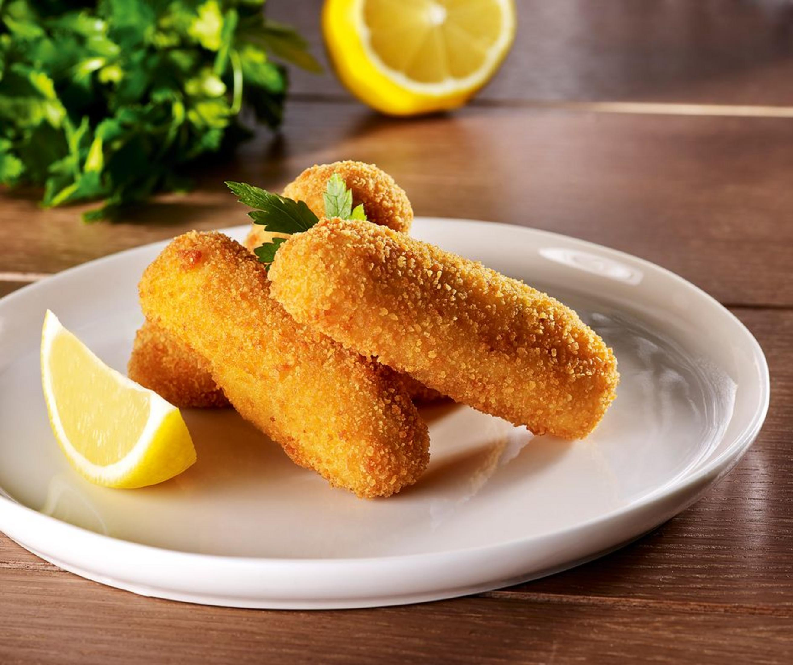 Chrupiące paluszki rybne na białym talerzu z cytryną i pietruszką.
