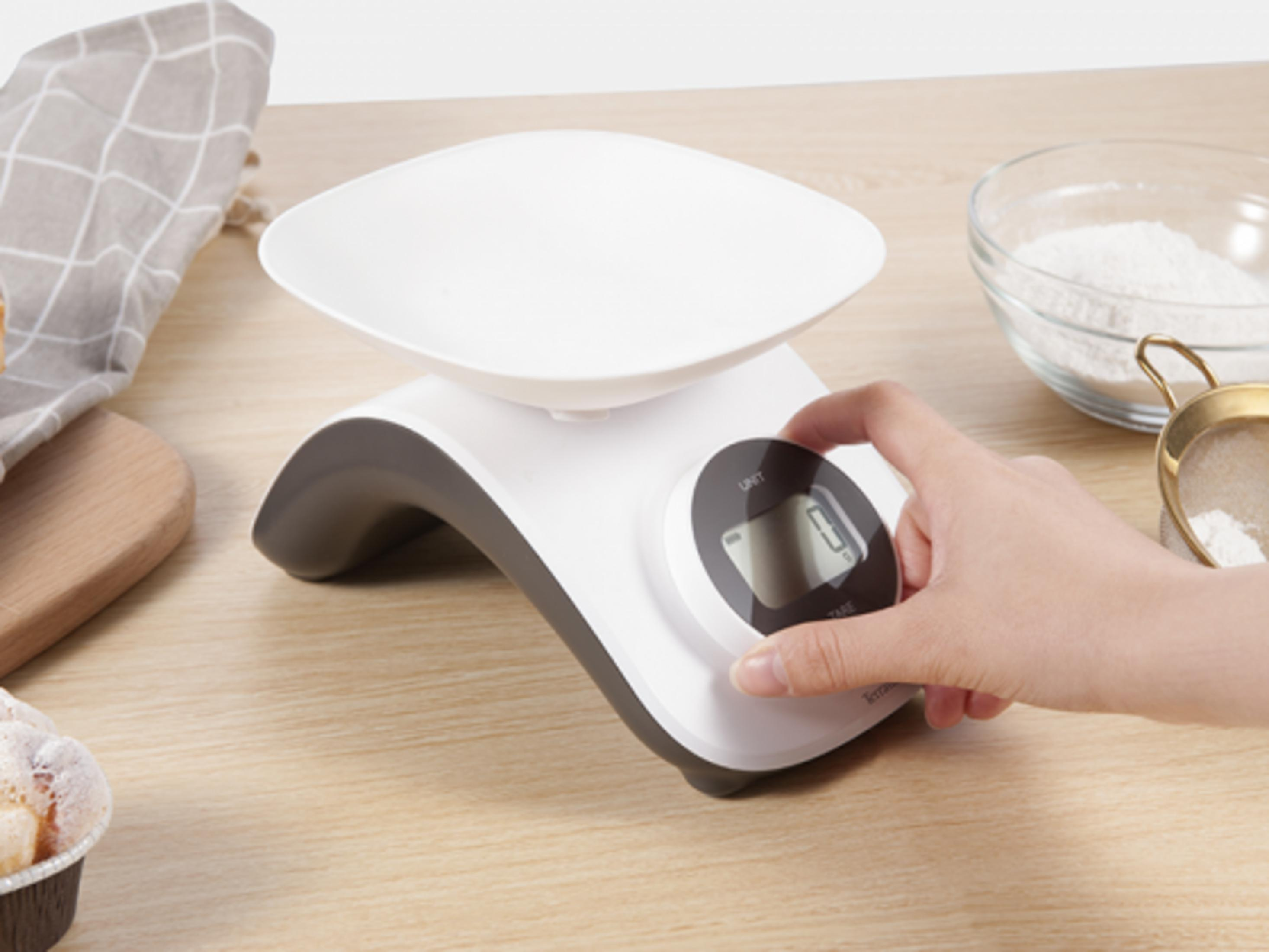 Una báscula de cocina digital blanca con una mano presionando un botón.