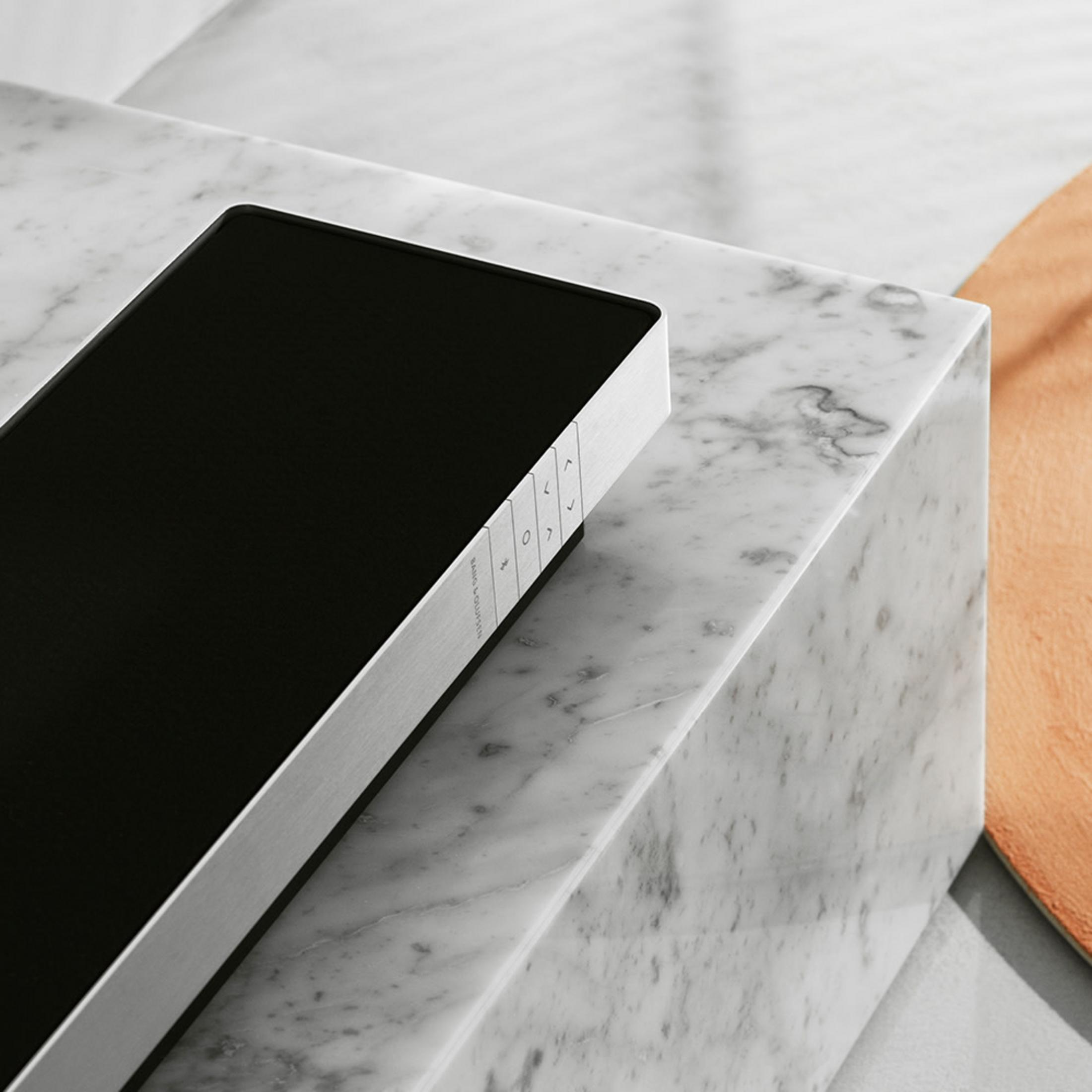 Czarny głośnik z srebrną krawędzią na marmurze.