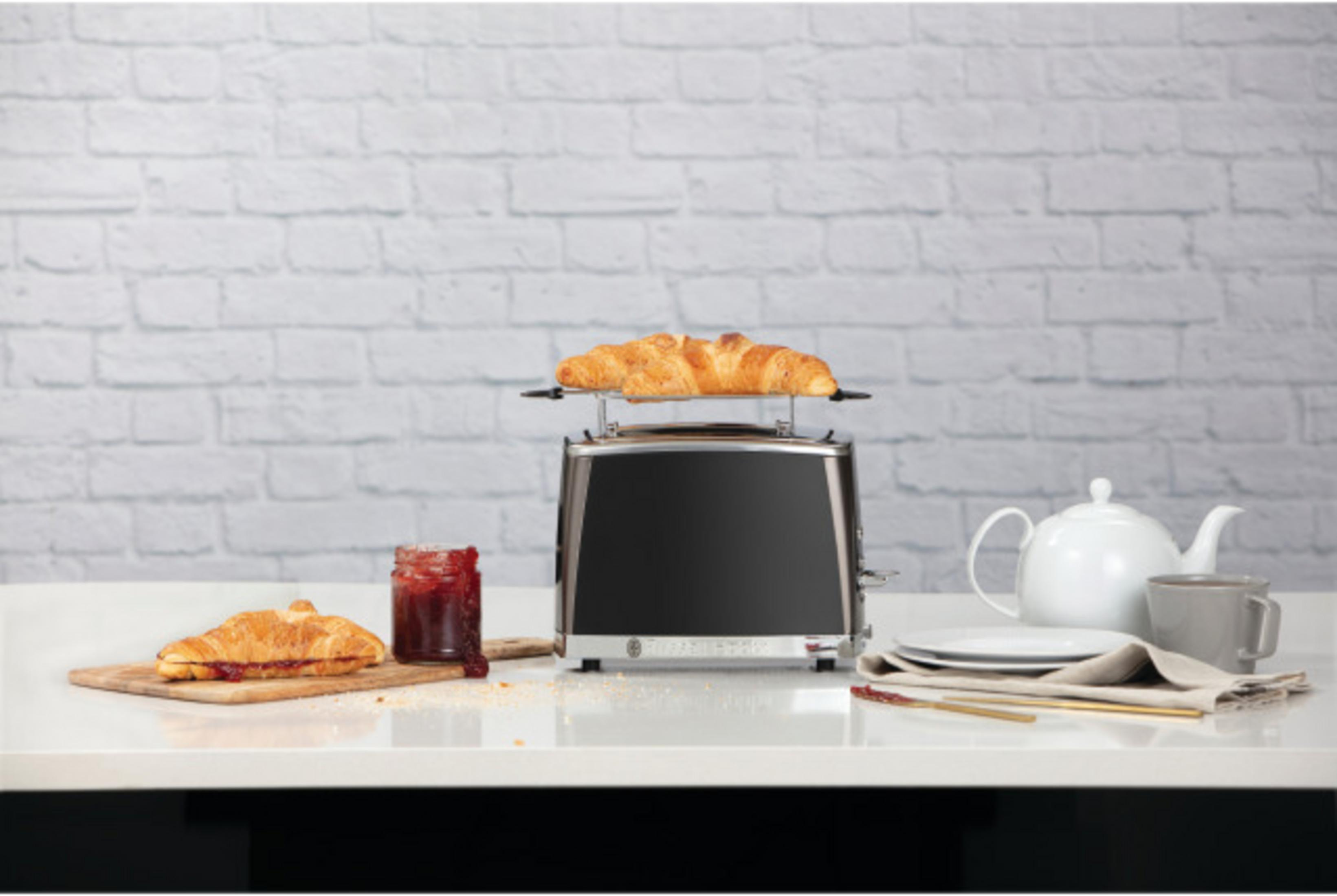 Ein Toaster mit Croissants, Marmelade, Teekanne und Tasse auf einem Tisch.
