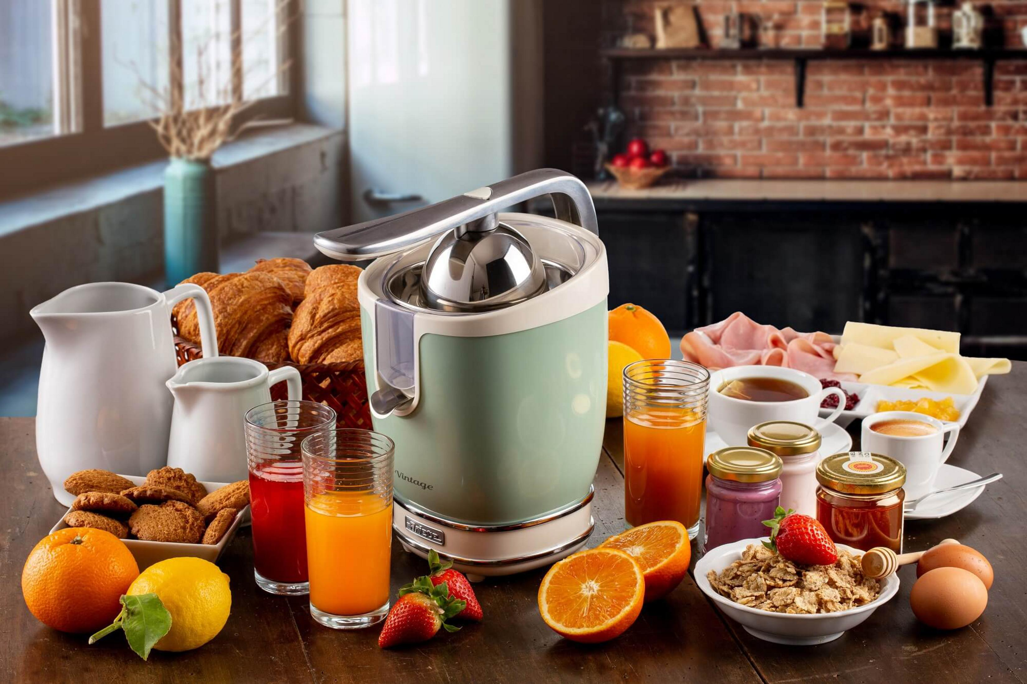 Stół śniadaniowy z wyciskarką do soków, croissantami, owocami, płatkami, jajkami, kawą.